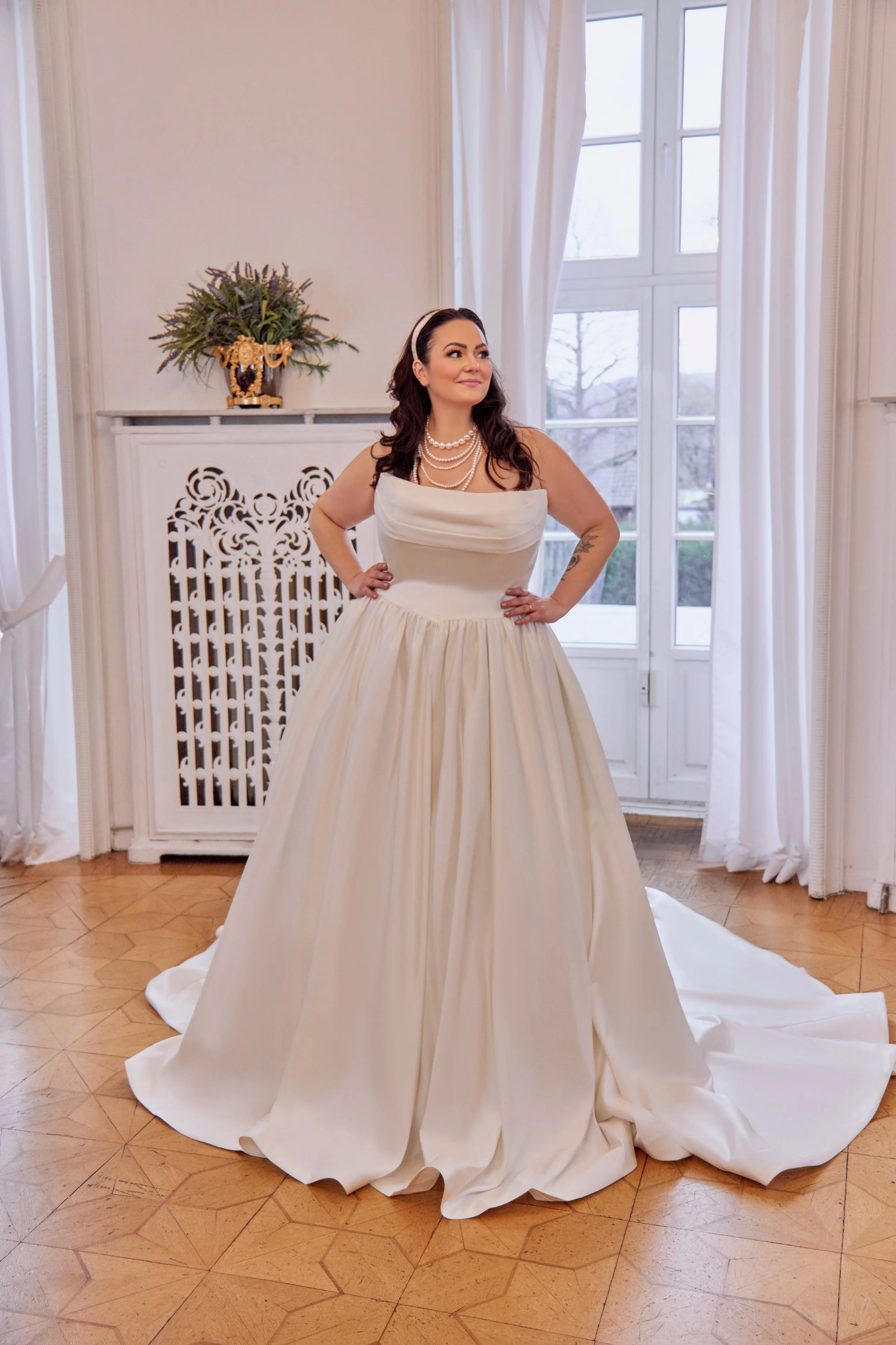 Full-length front view of Lia Bella Model Tila, a curvy satin ball gown with a draped cowl neckline and pointed basque waist.