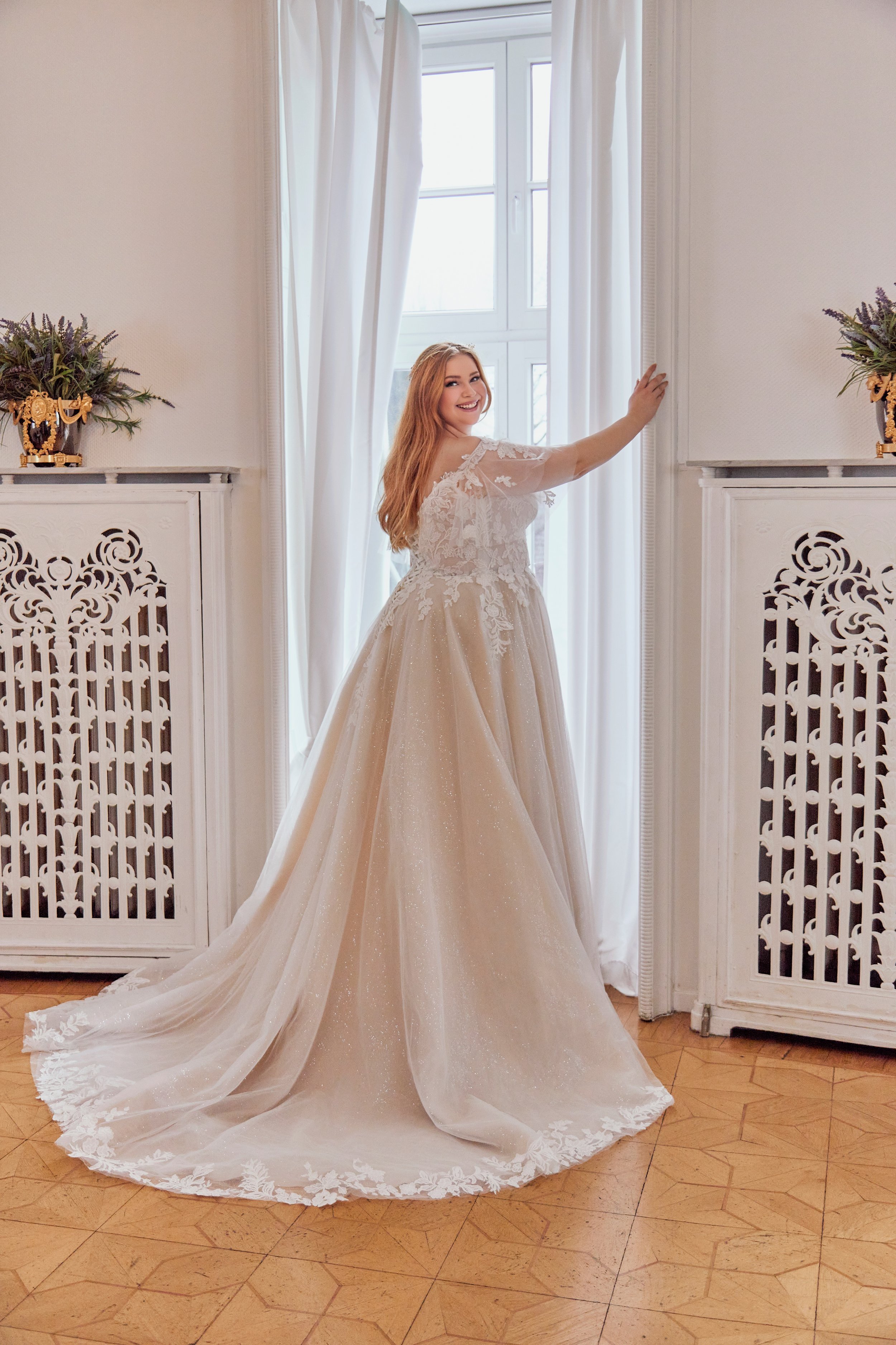 Three-quarter back view of Lia Bella Model Tewa showing the illusion lace back, shimmering A-line skirt and lace-edged chapel train.