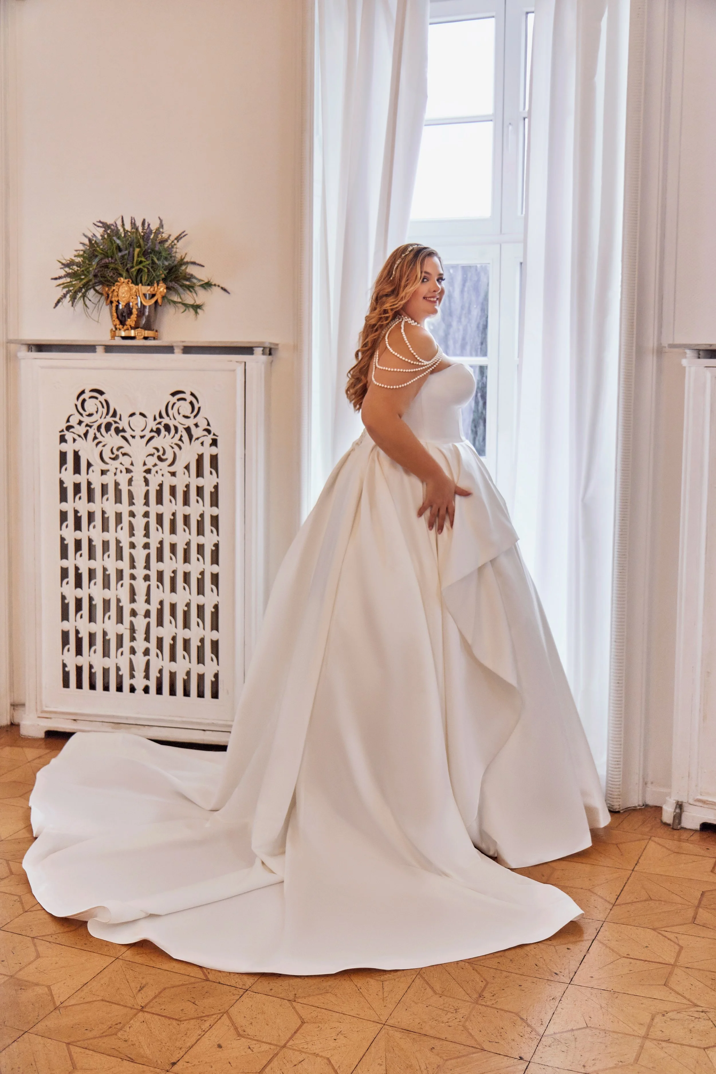 Three-quarter view of Lia Bella Model Taty showing the draped overskirt and wide chapel train in structured satin.