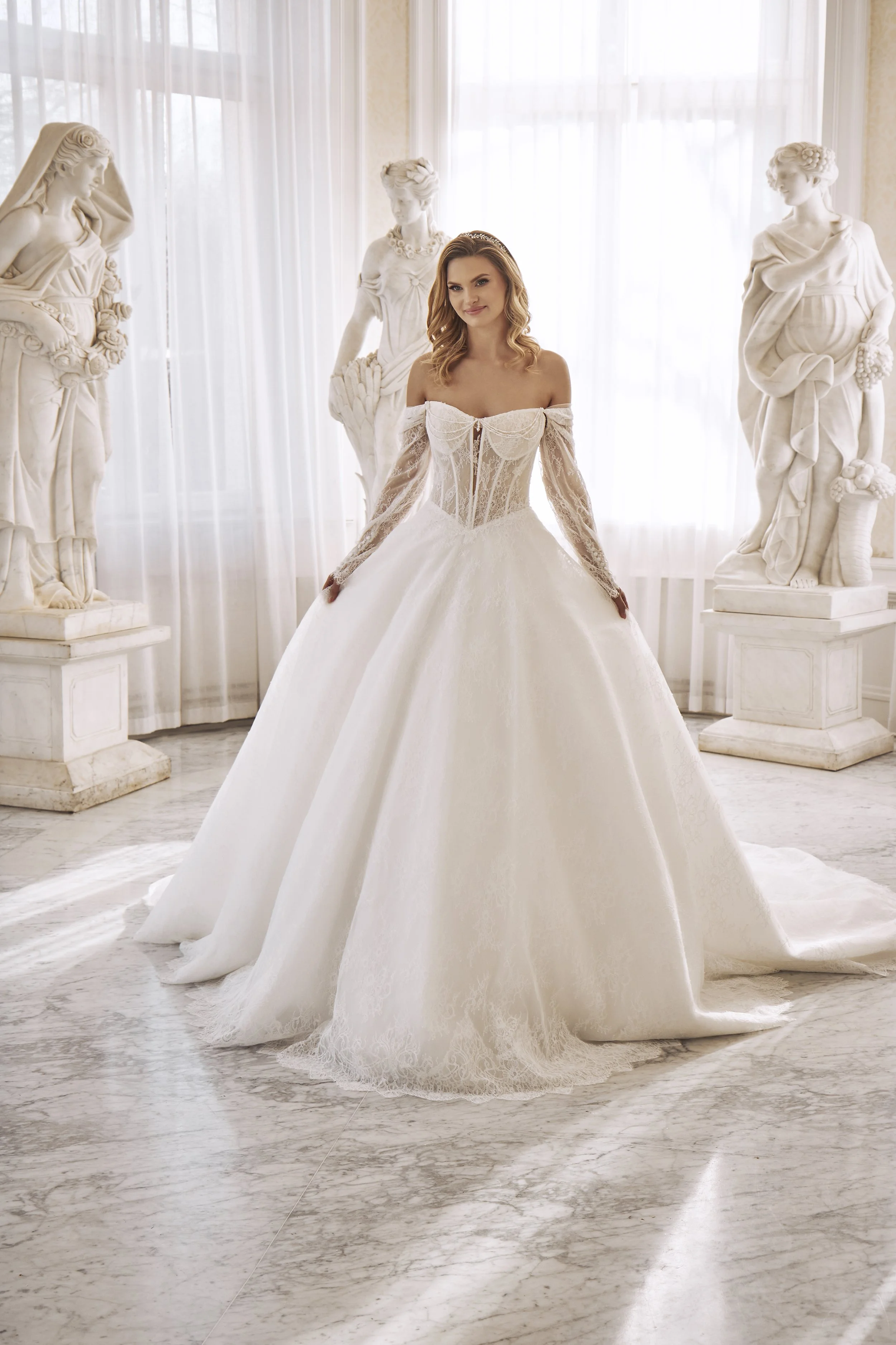 Full front view of Lia Bella Model Tia, an off-the-shoulder lace ball gown wedding dress with long illusion sleeves.