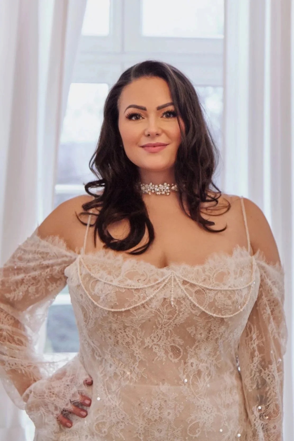 Front bodice view of Lia Bella Model Tiffania featuring delicate all-over lace, pearl draping and long transparent sleeves.