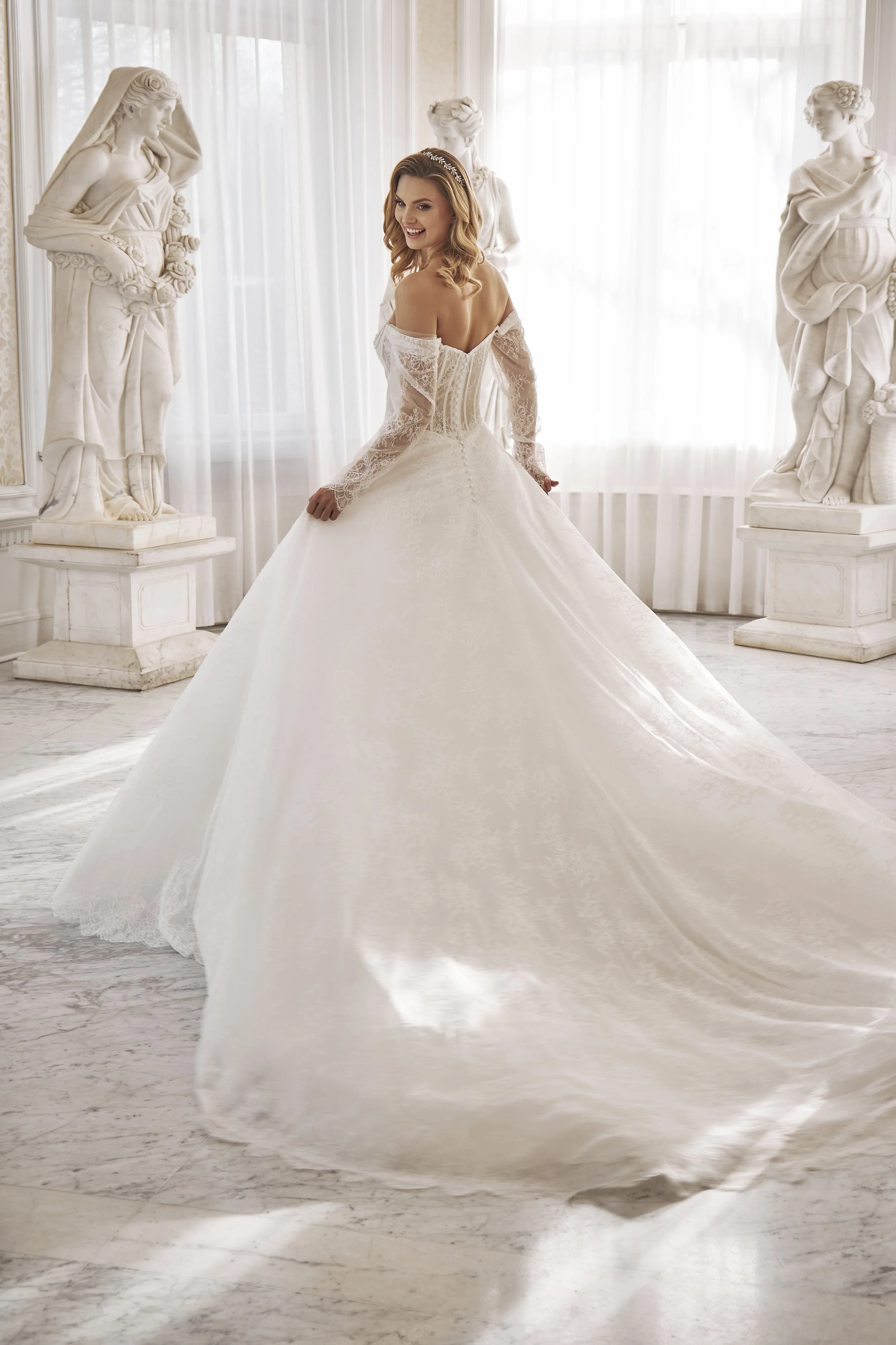 Back view of Lia Bella Model Tia featuring a low V-back, sheer corset structure and extended lace chapel train.