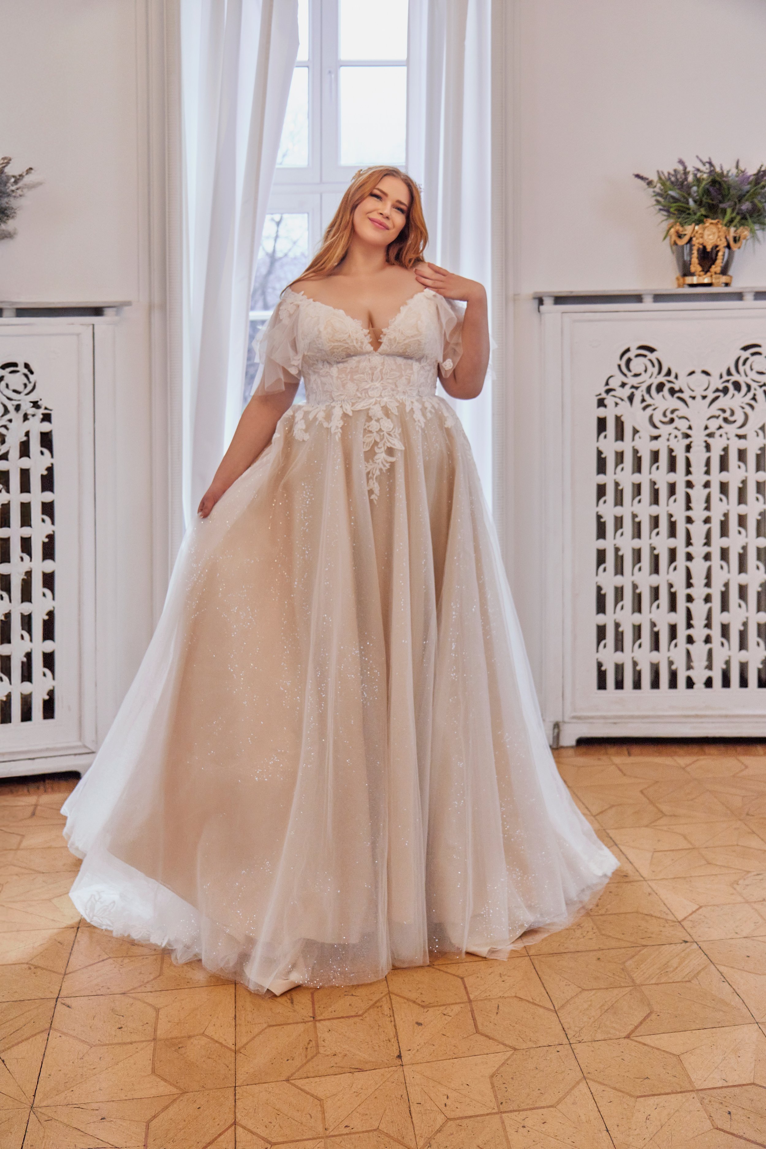 Full front view of Lia Bella Model Tewa, a curvy A-line wedding dress with a floral lace bodice, flutter sleeves and shimmering tulle skirt.