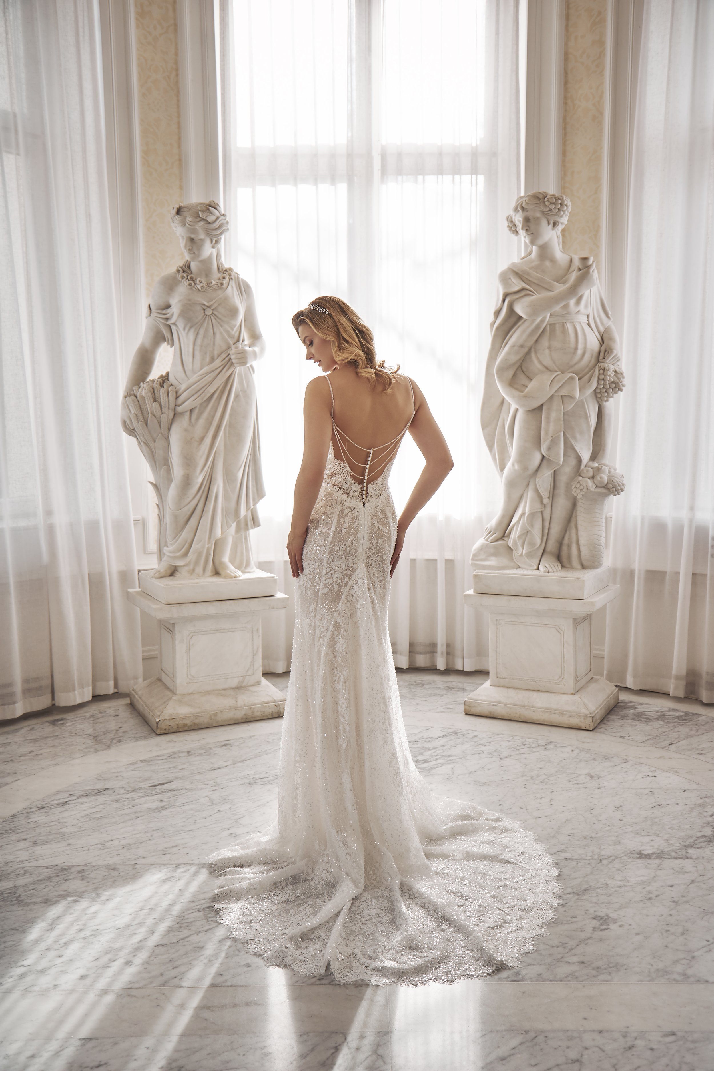 Back view of Lia Bella Model Tamra with a low open back, draped beading, covered buttons and a lace train.