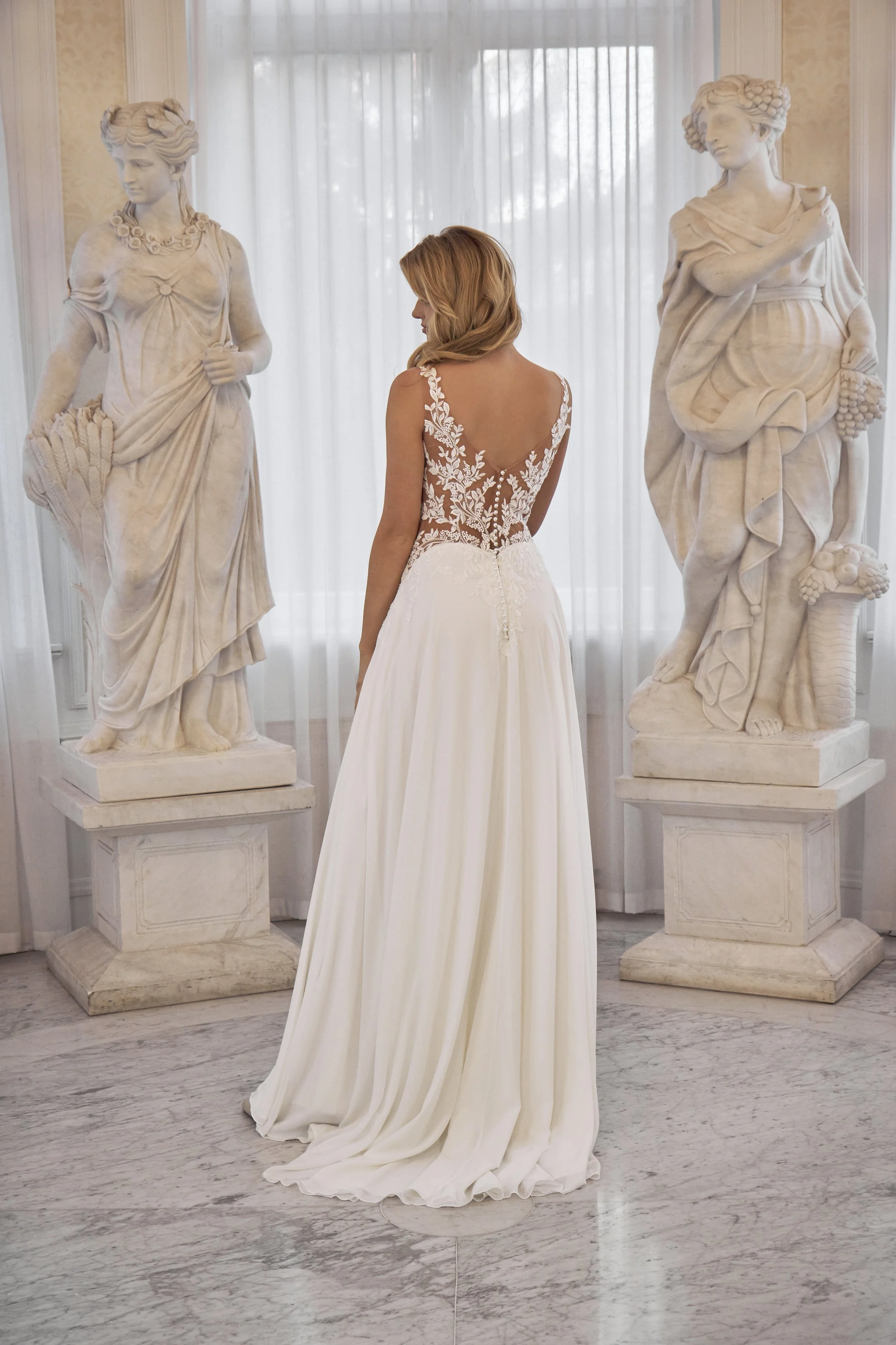 Full back view of Lia Bella Model Tommy showing the deep V-shaped illusion lace back, covered buttons and flowing chiffon skirt.