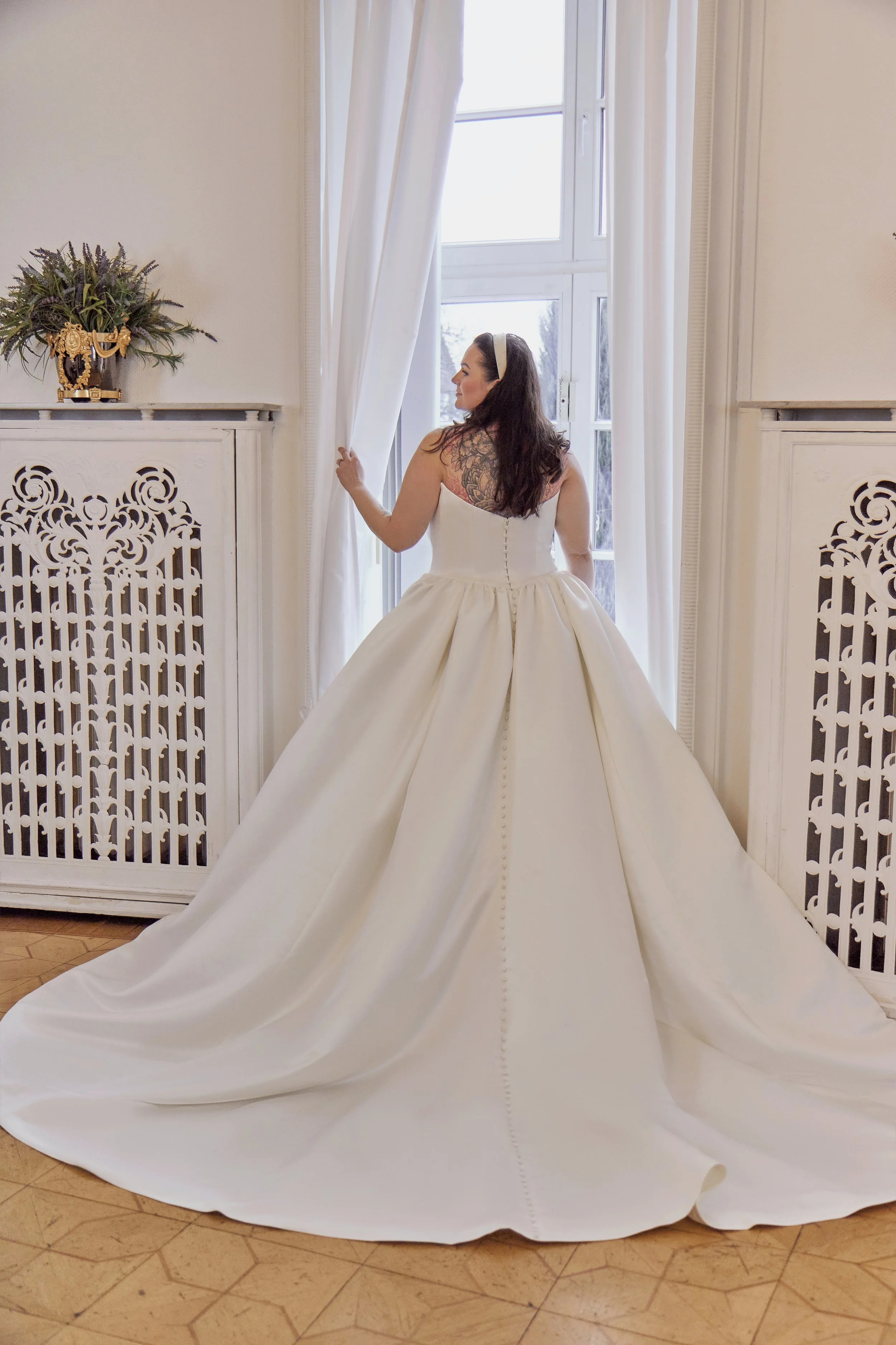 Back view of Lia Bella Model Tila showing the low satin bodice, covered buttons and wide chapel train.