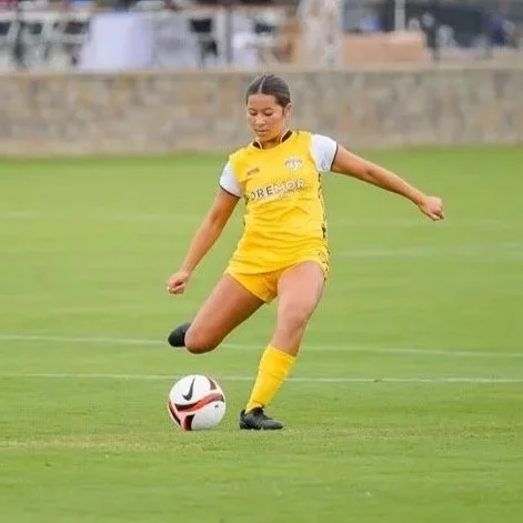 Female soccer player kicking a soccer ball on a grassy field