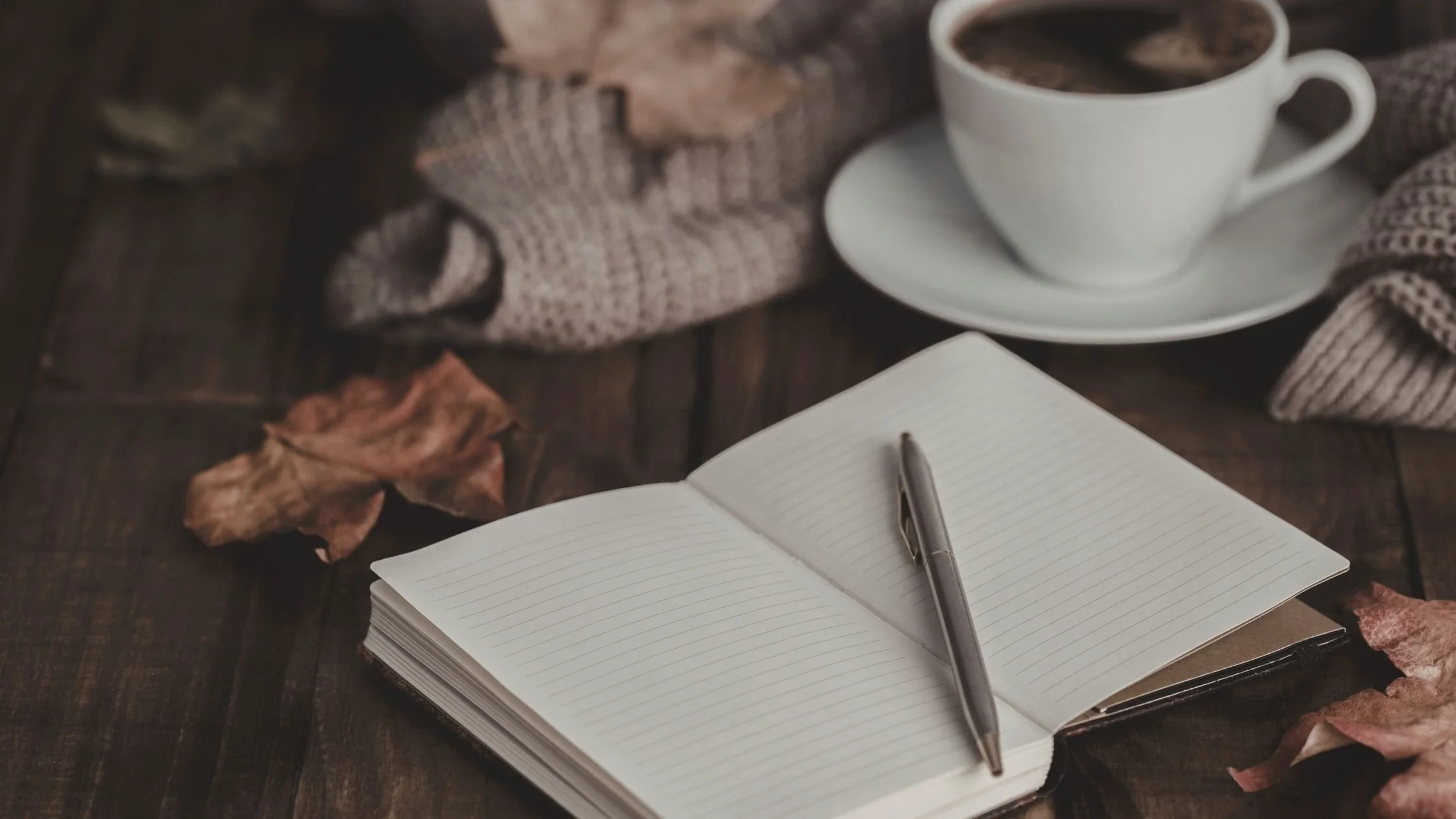 Open bullet journal on a desk with handwritten notes, alongside a pen and a coffee cup, representing simple productivity and analogue planning for business organisation