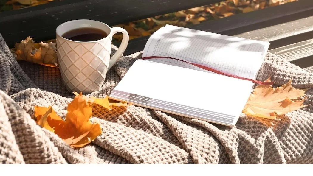 A garden bench with a blanket, a mug of coffee, a notebook and fallen autumn leaves, representing a business reset.