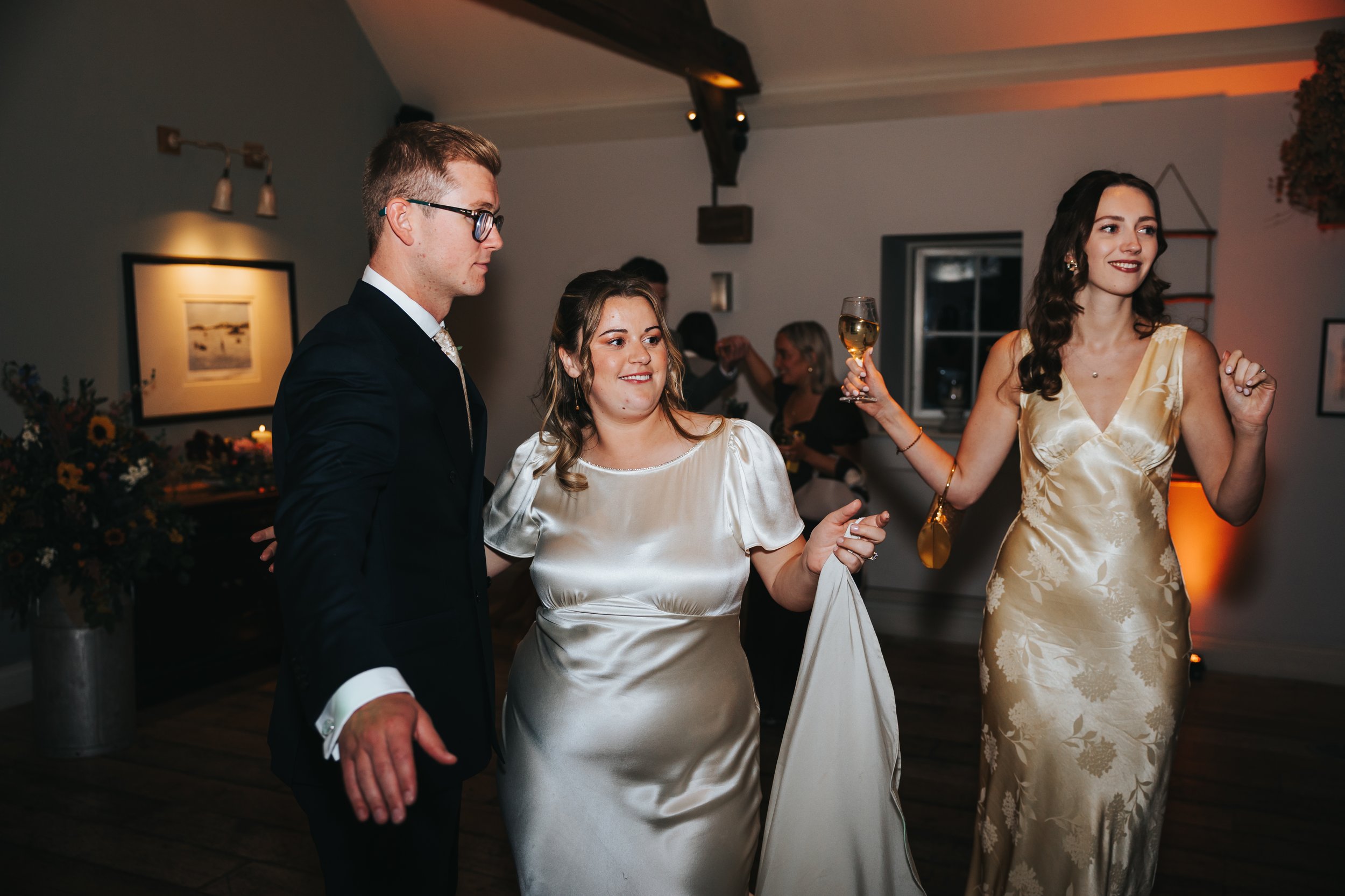 People dancing at a wedding reception, with one woman holding a glass of champagne and smiling.