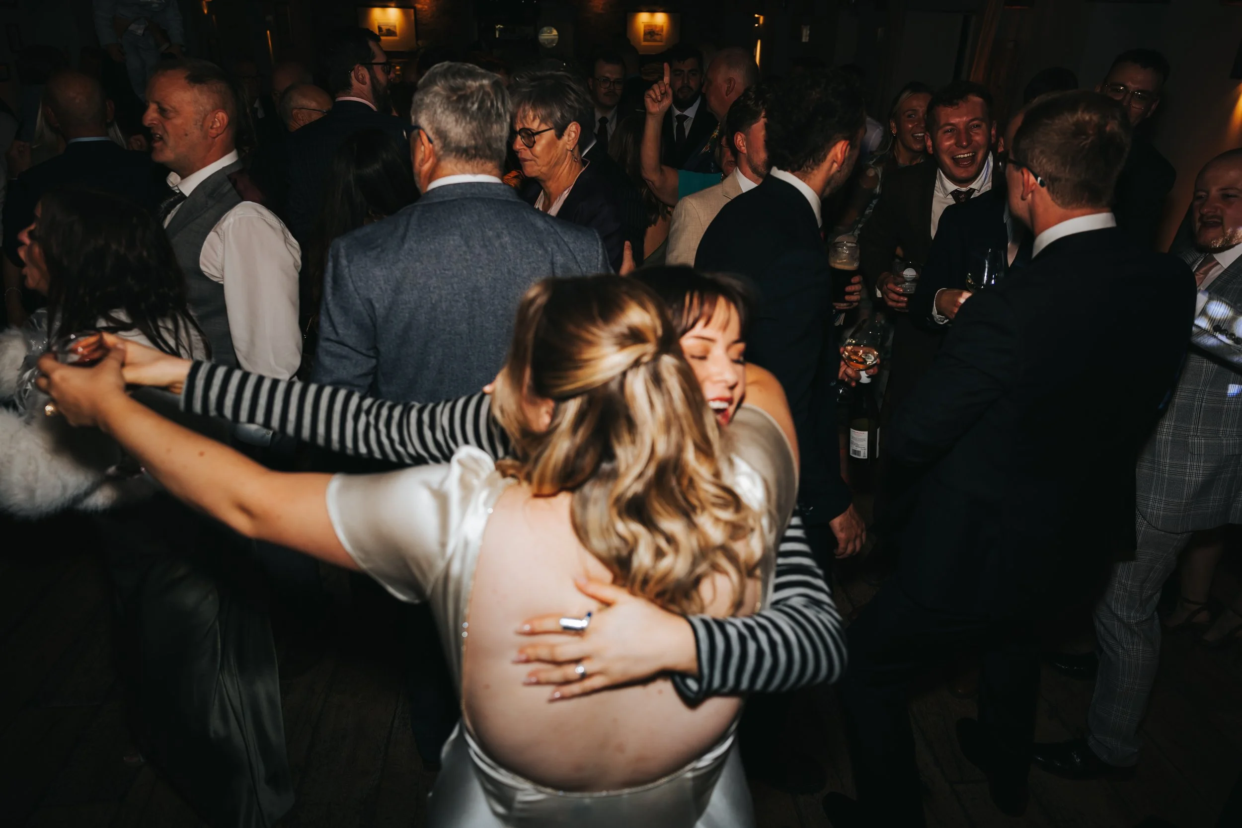 People dancing and celebrating at a lively party, with some holding drinks and smiling.
