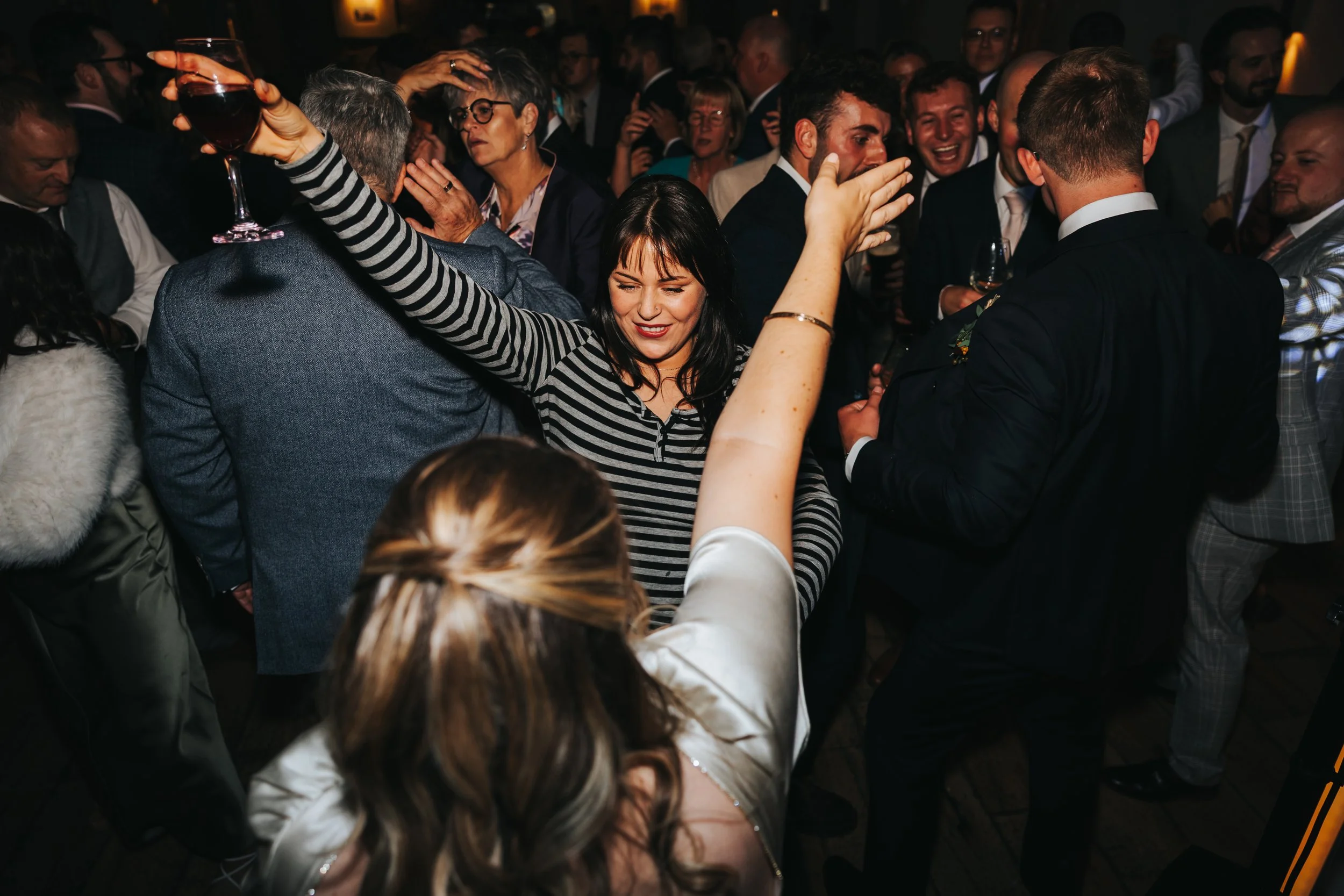 People dancing and socializing at a lively party or celebration with dim lighting and a crowded atmosphere.
