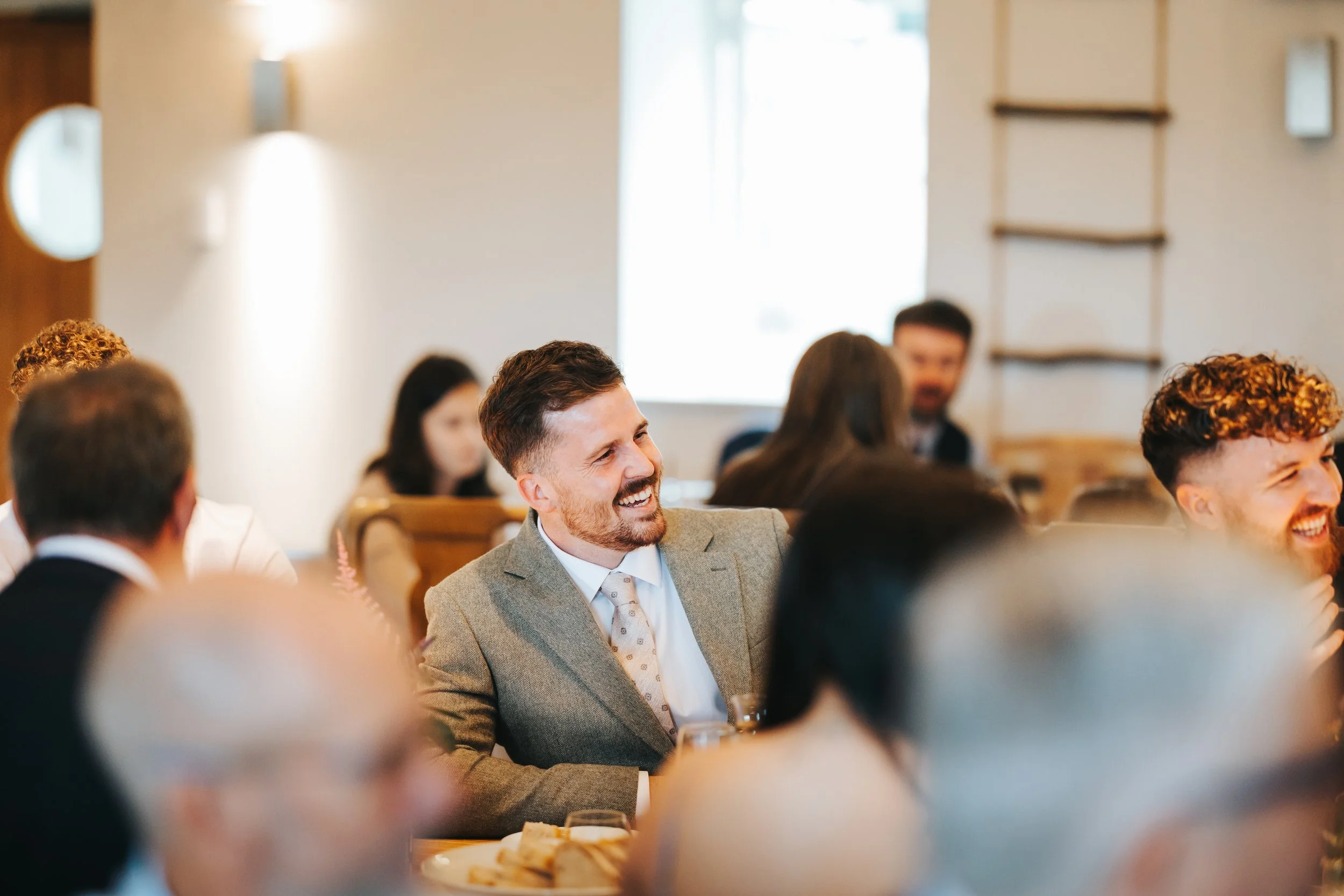 People sitting at tables in a well-lit, indoor space, smiling and enjoying a social or professional event.