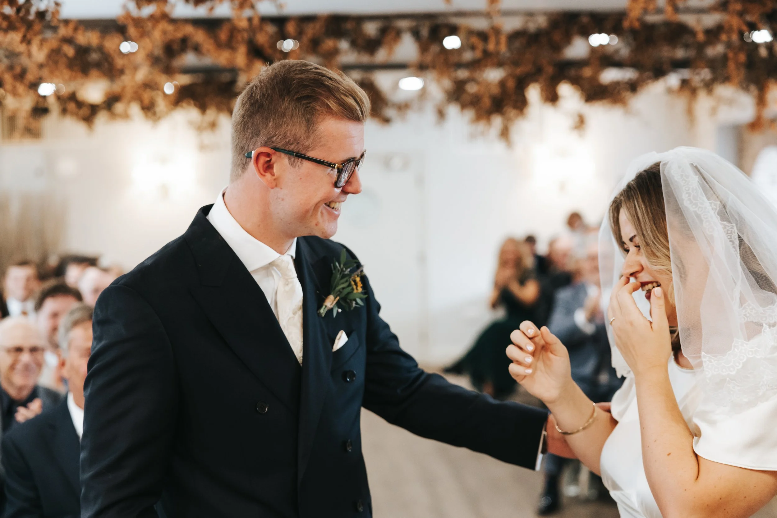 A groom and bride sharing a joyful moment during a wedding ceremony, with guests in the background.