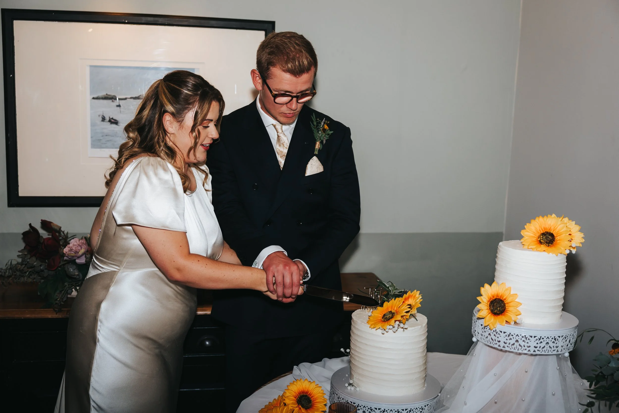 A bride and groom cut a wedding cake decorated with sunflowers.