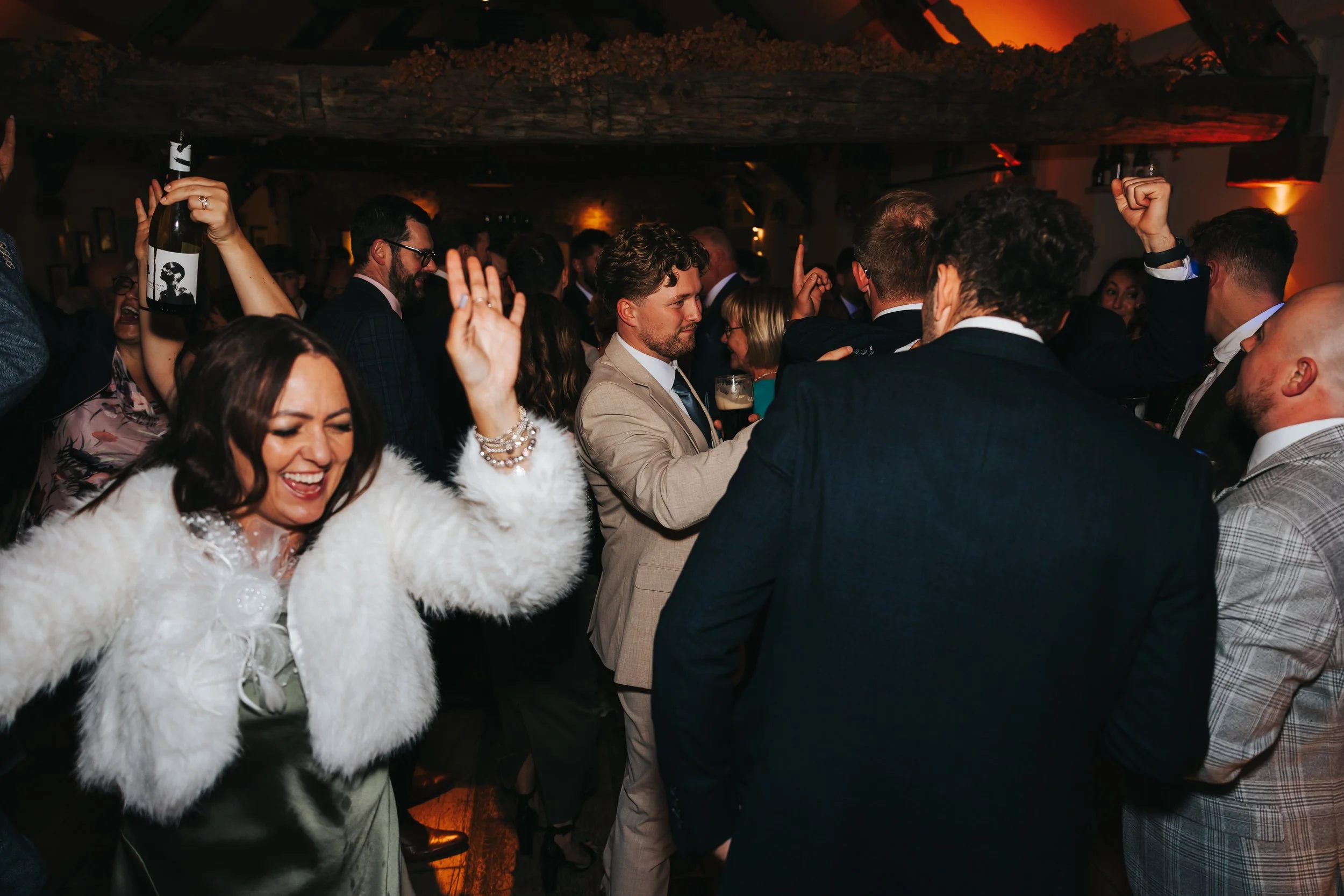 People dancing and celebrating at a lively party or wedding reception in a warmly lit indoor venue.