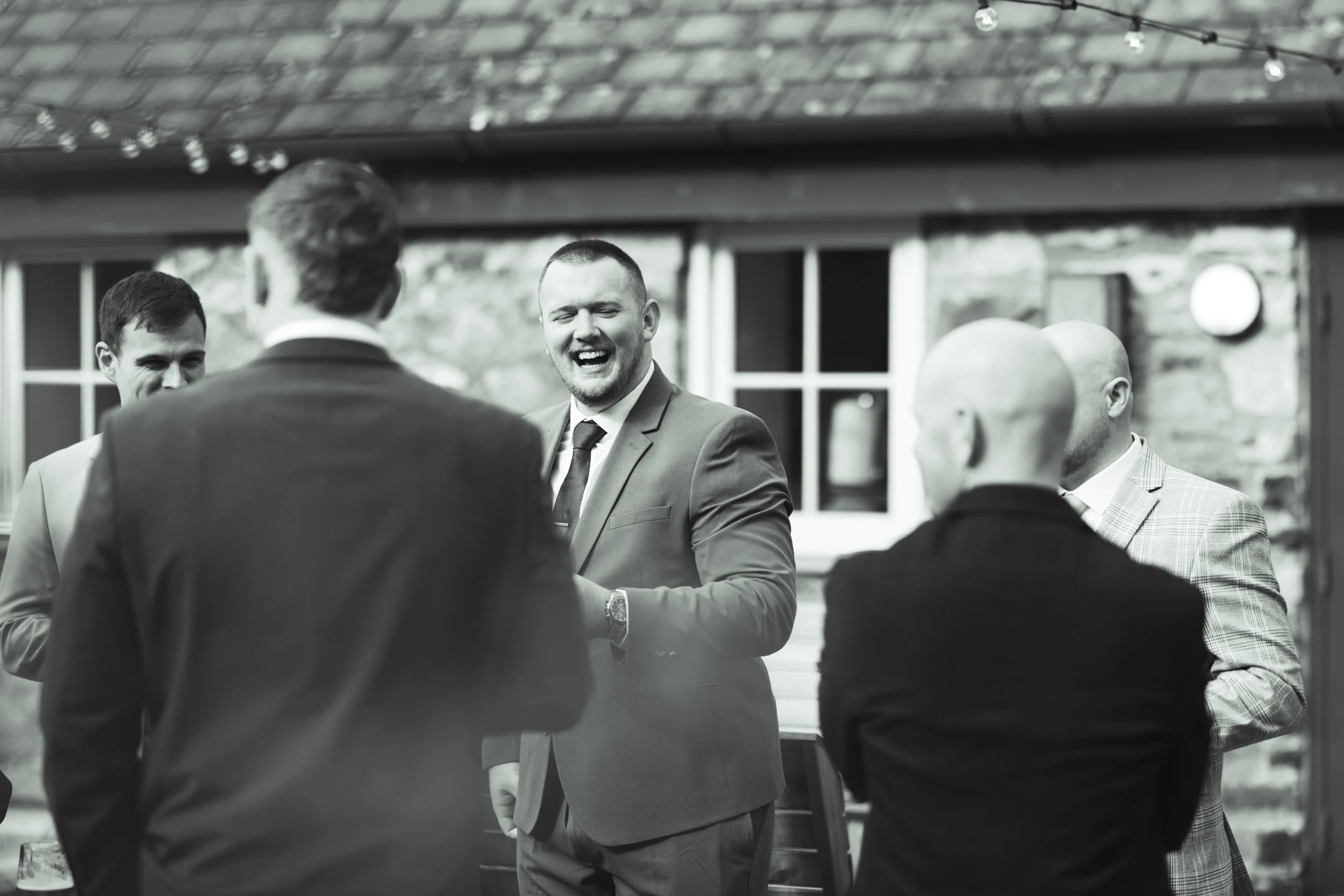 Group of men in suits socializing and laughing outside at a gathering.