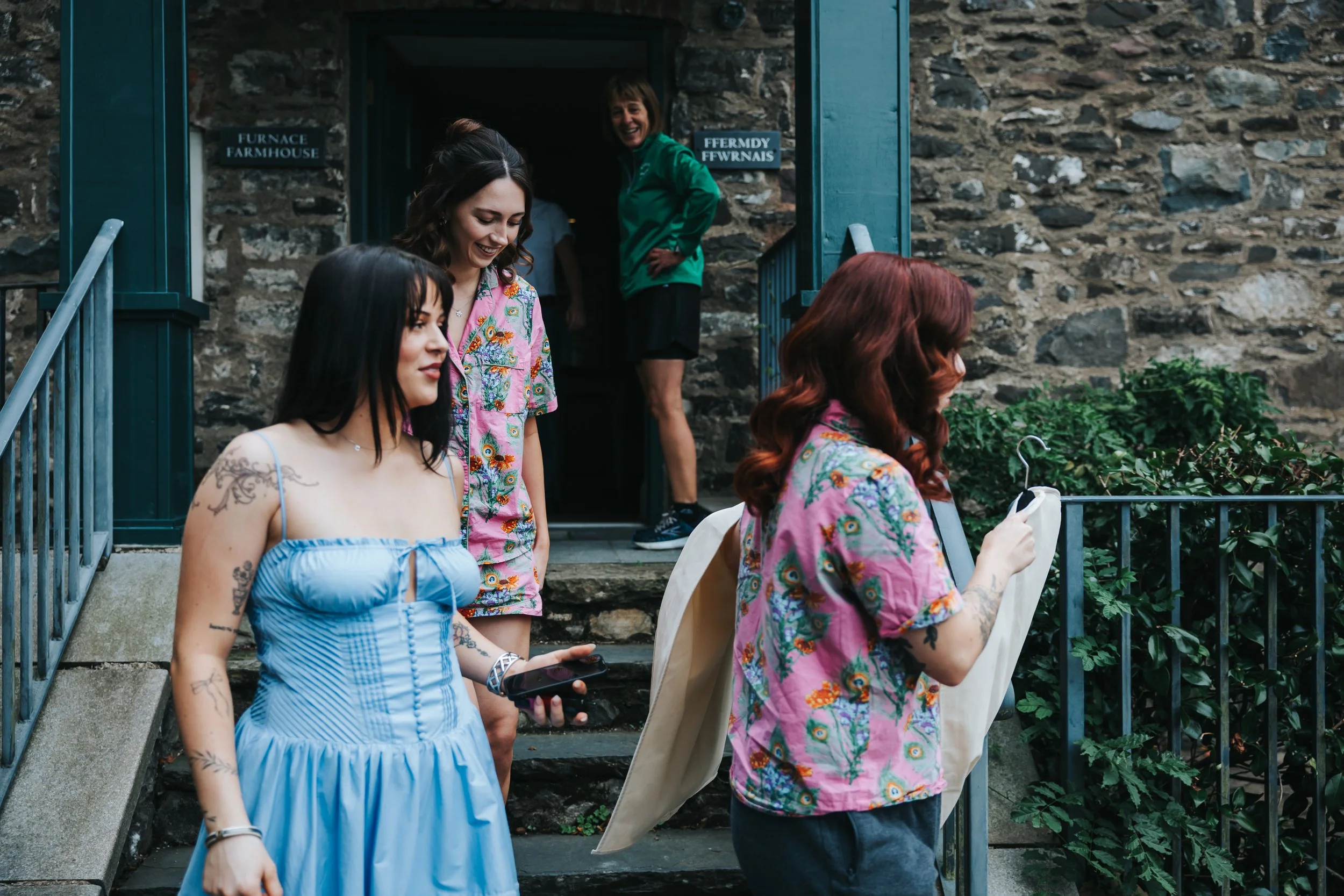 Group of women walking down stone steps outside a stone building with blue trim, some looking at their phones, one smiling at the camera, and a woman in the background smiling at the door.