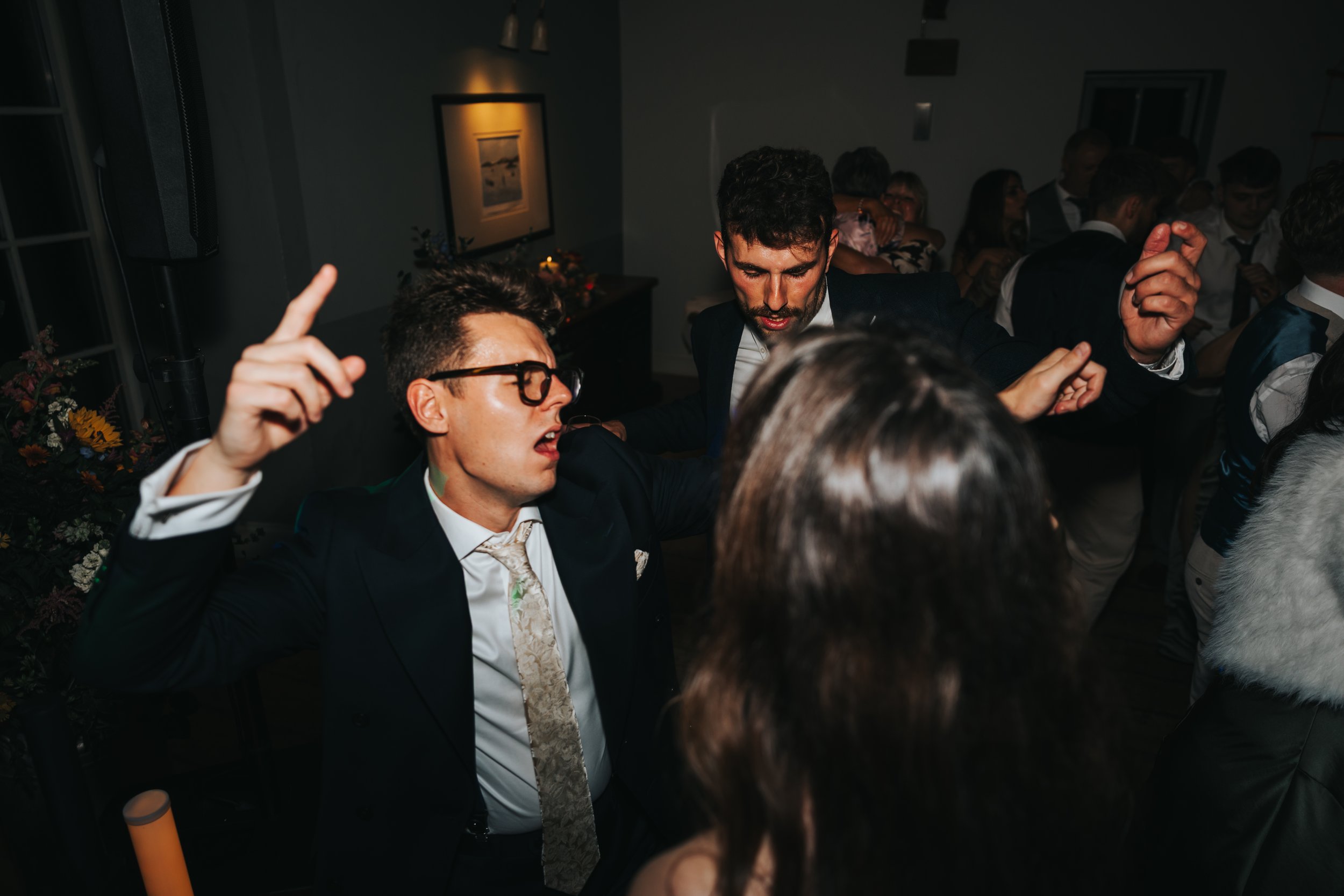 People dancing and celebrating at an indoor event or party, with some individuals raising their hands and enjoying the music.