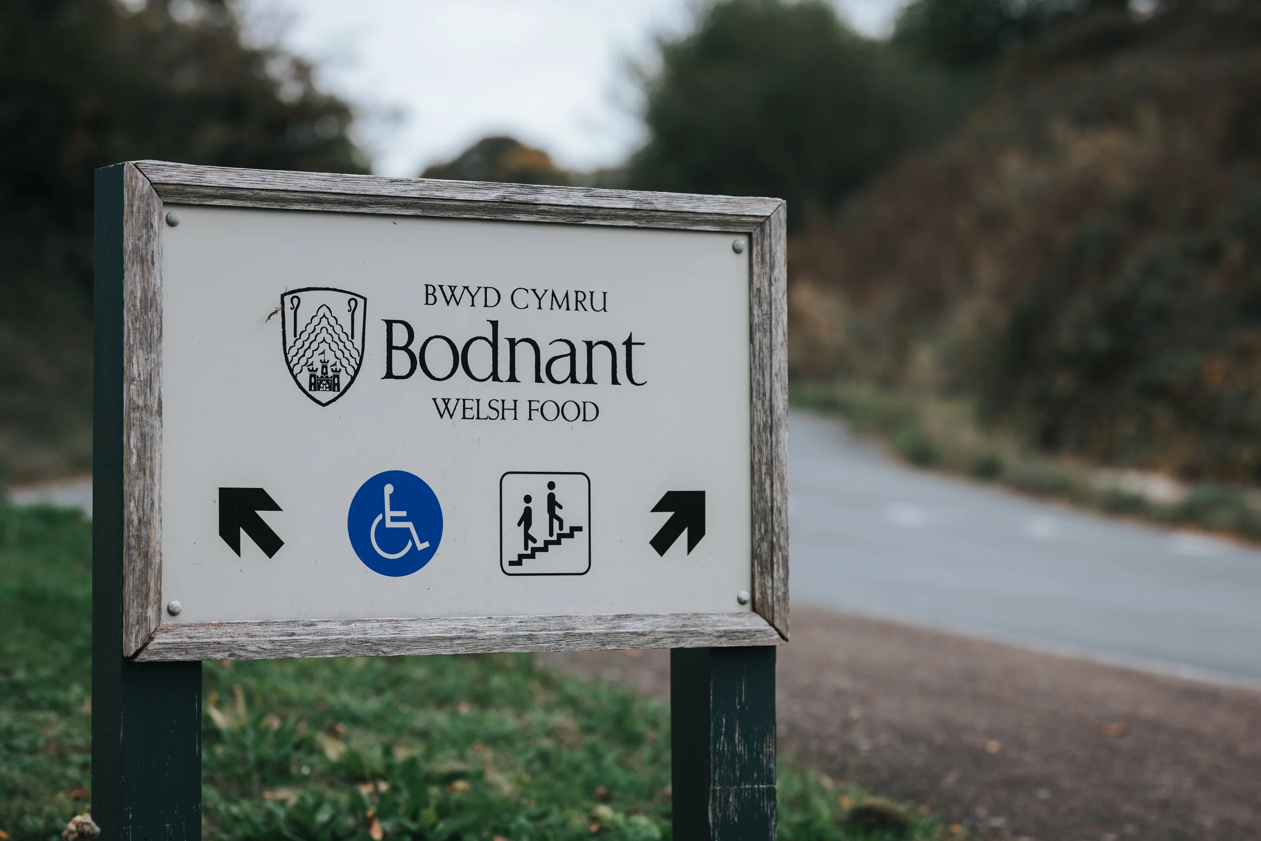 Sign for Bodnant Welsh Food with symbols for wheelchair accessibility, stairs, and directions to the left and right.