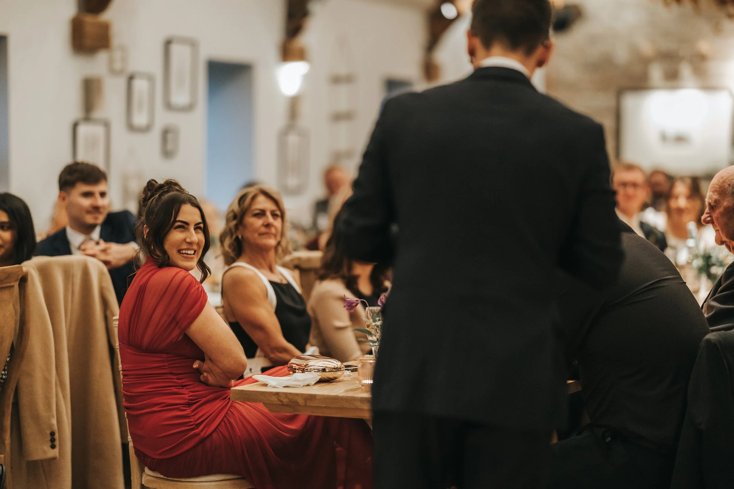 People seated at a formal dinner event, with a woman in a red dress smiling and looking towards the front.