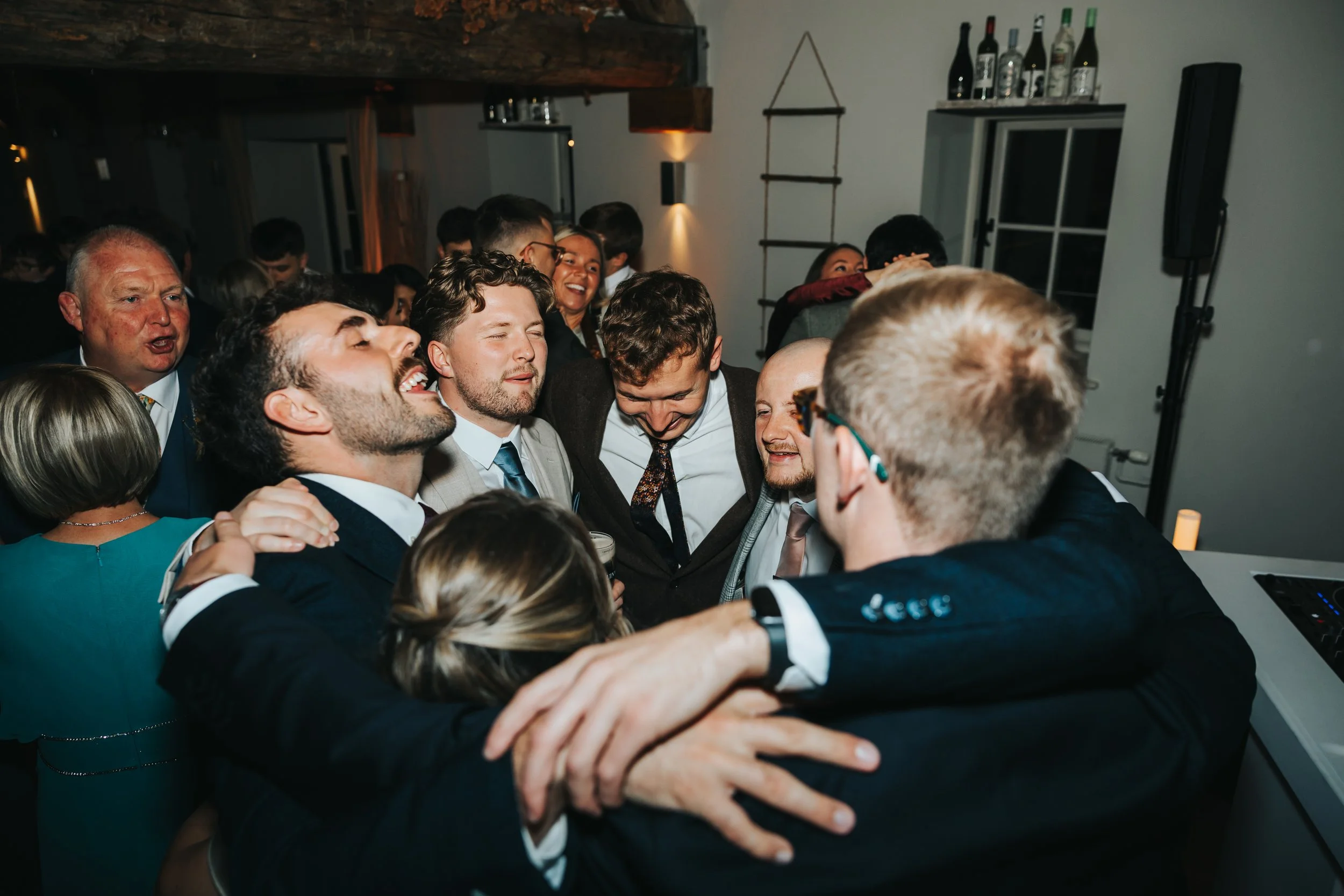 Group of people at a party, hugging and smiling together in a lively indoor setting.