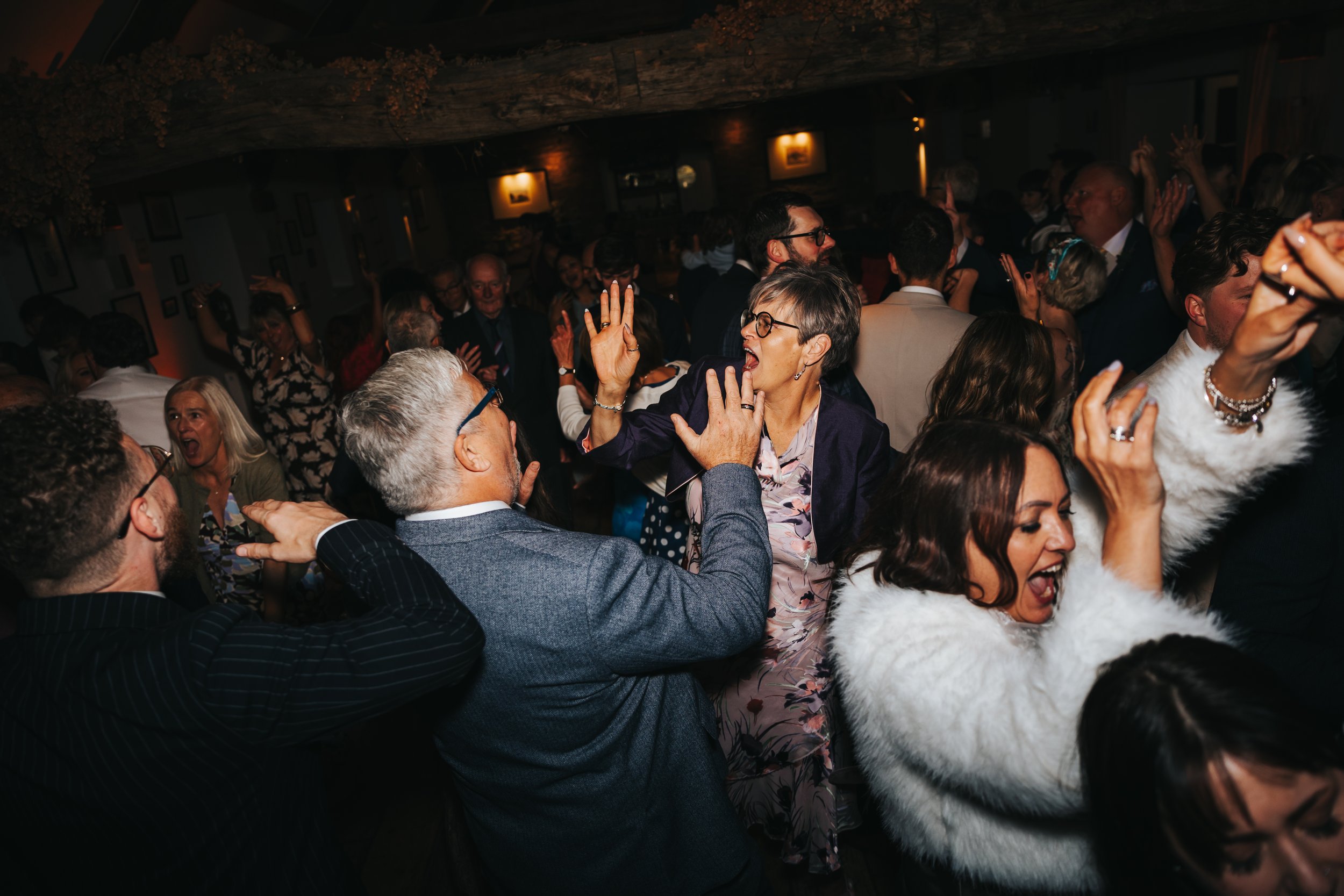 People dancing and celebrating at a lively social gathering or party with dim lighting and wooden beams.