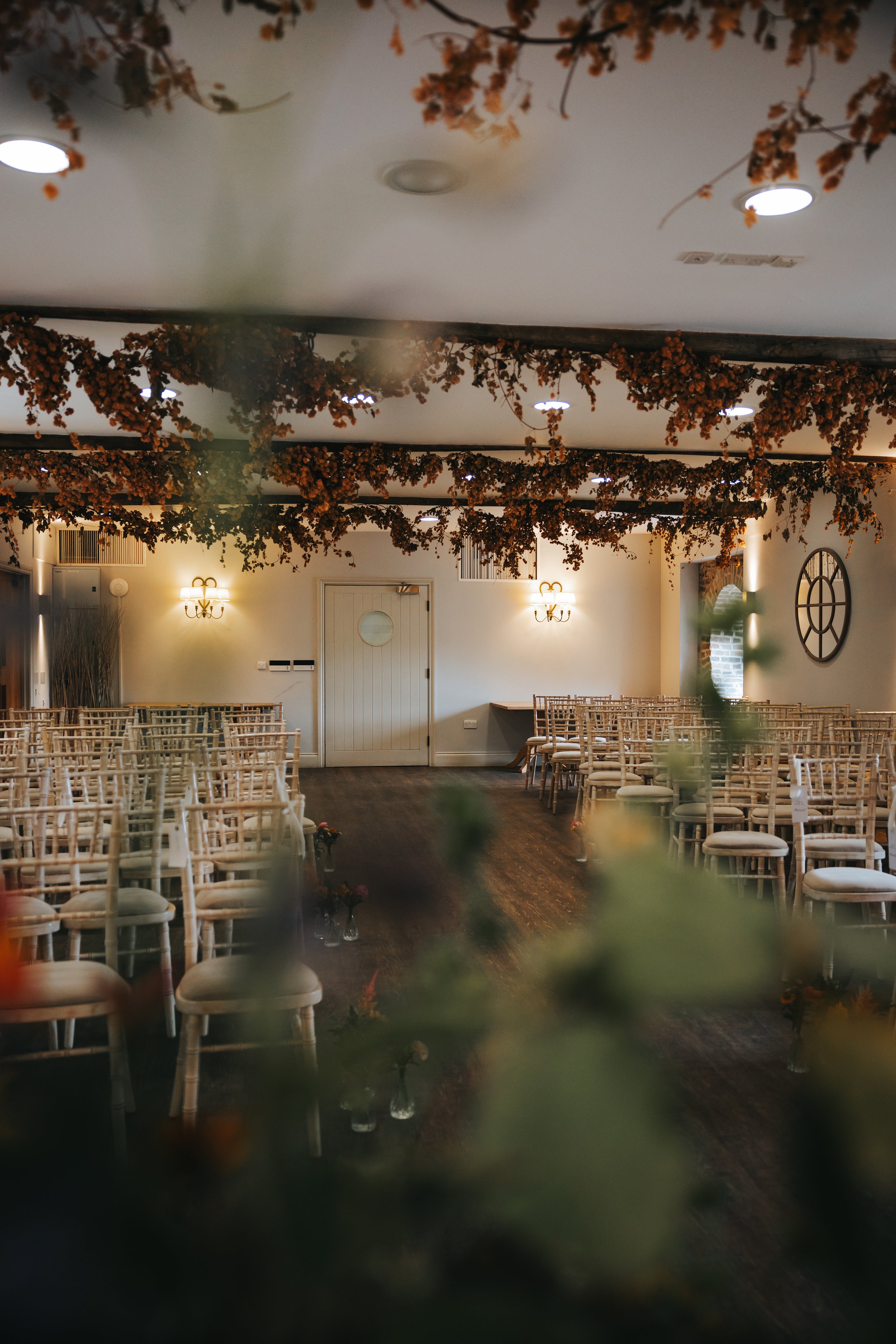An empty wedding ceremony room with rows of white chairs, floral decorations hanging from the ceiling, and soft lighting.