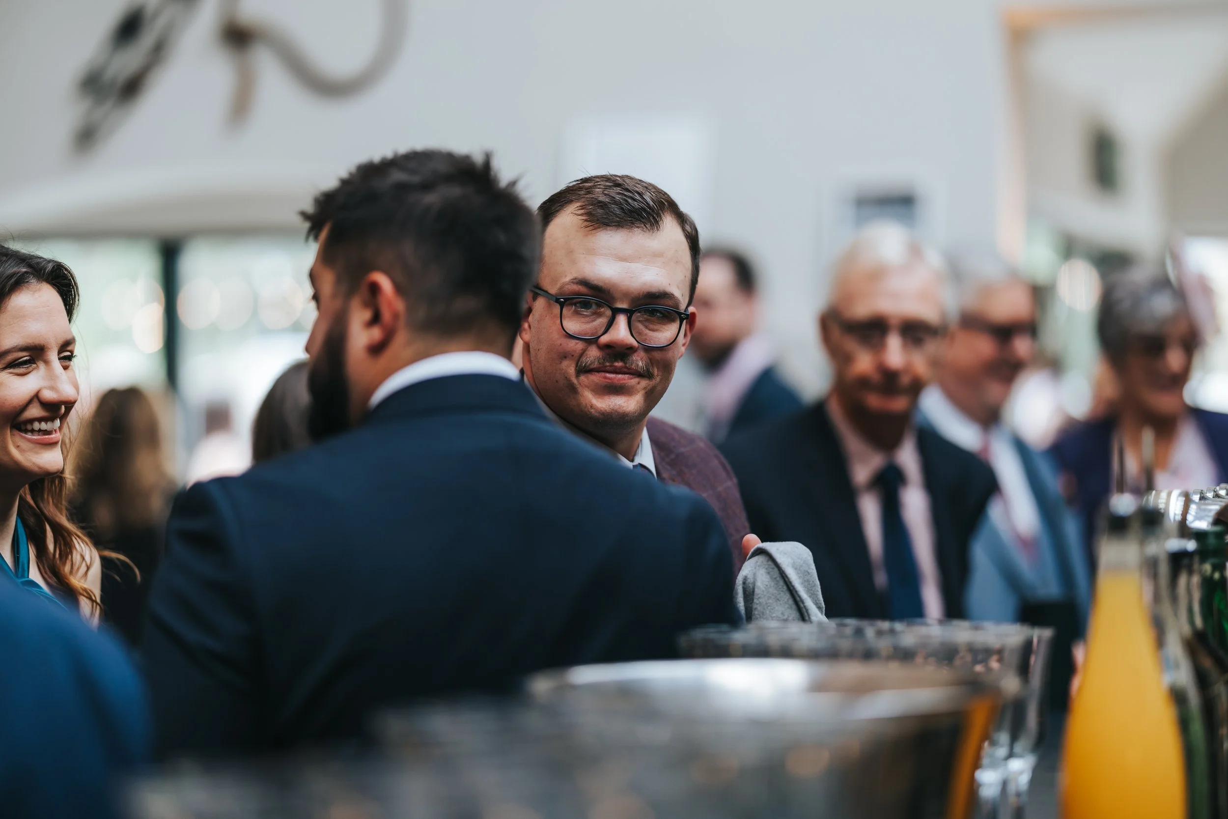 Group of professionally dressed people at a social event or conference, engaging in conversation with drinks and beverages on the table.