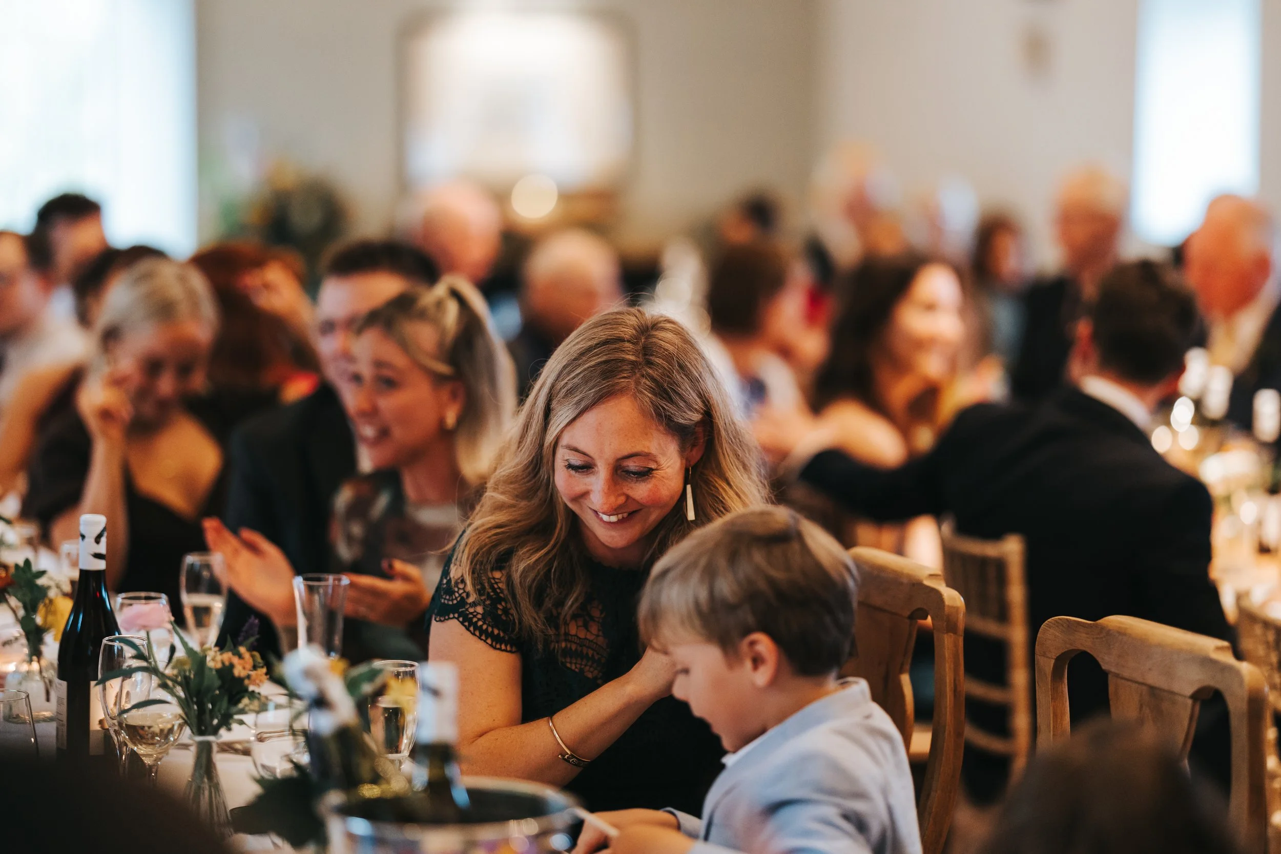 People seated at a banquet table in a formal setting, smiling and engaging with each other, with floral centerpieces and glasses on the table.