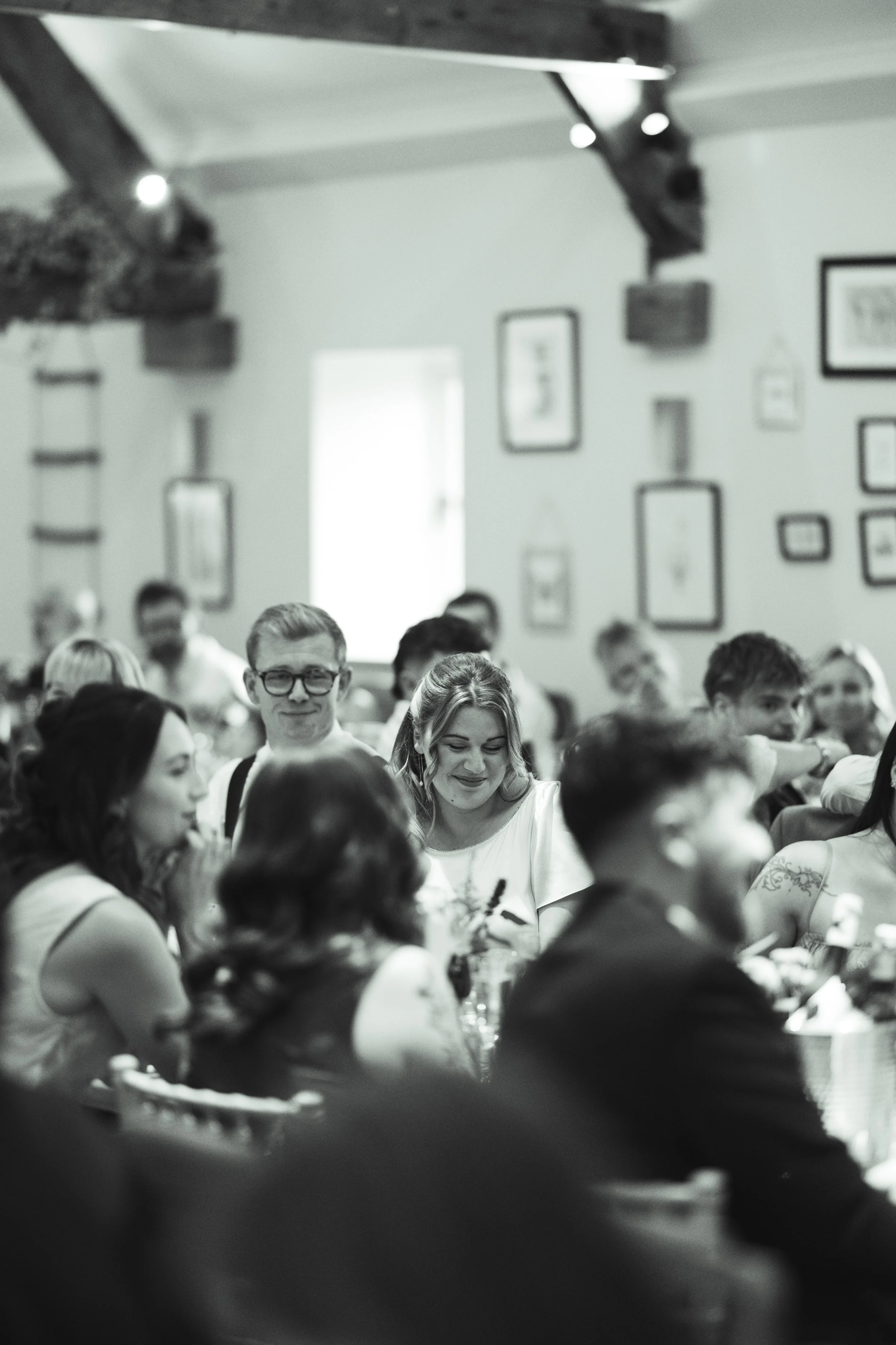 People sitting at a table in a restaurant or café, engaged in conversation and smiling, with framed pictures on the wall in the background.