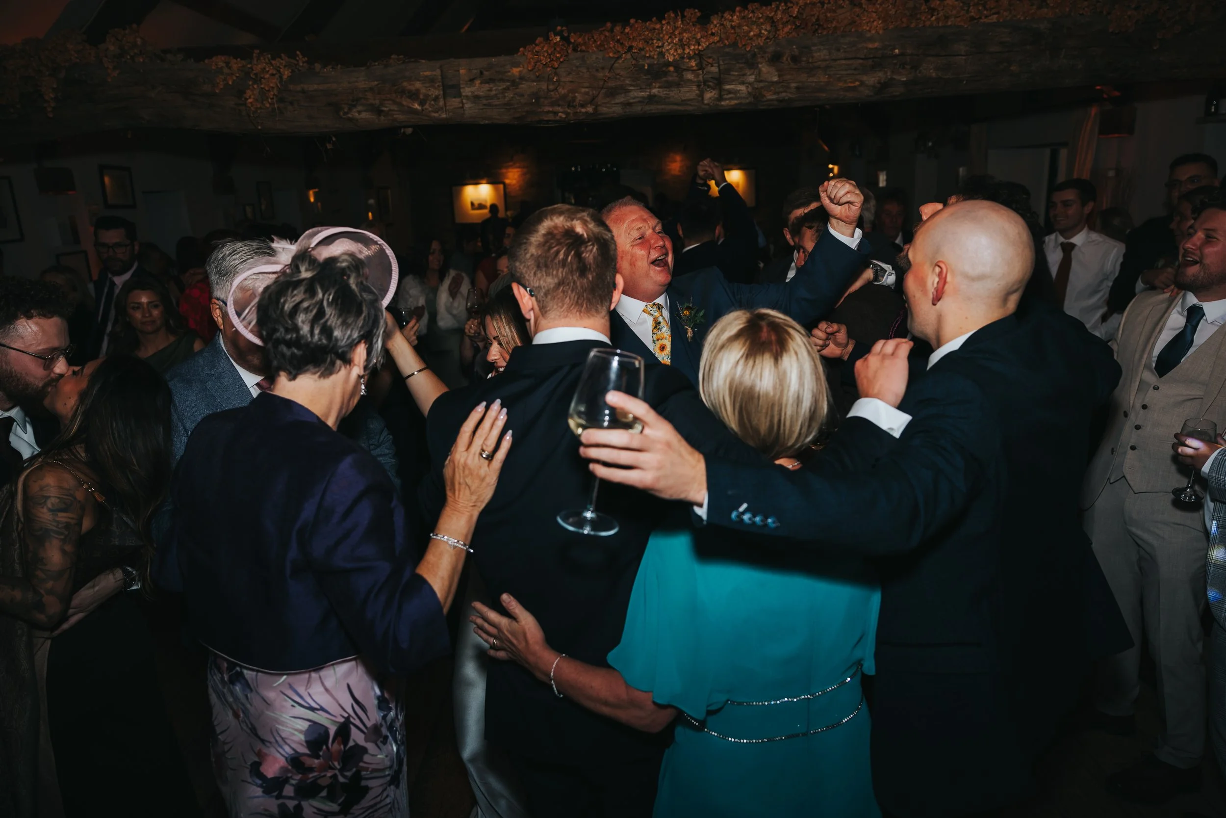 People dancing and celebrating in a dimly lit indoor space, at a joyful event or party, with some holding glasses.