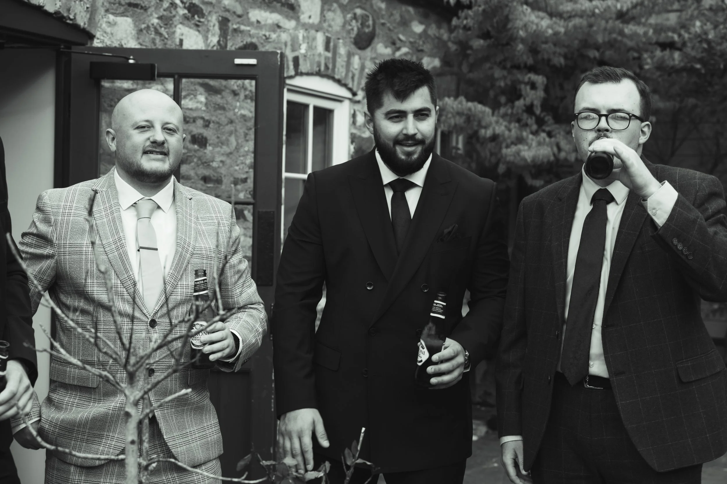 Three men in suits holding drinks at an outdoor gathering.