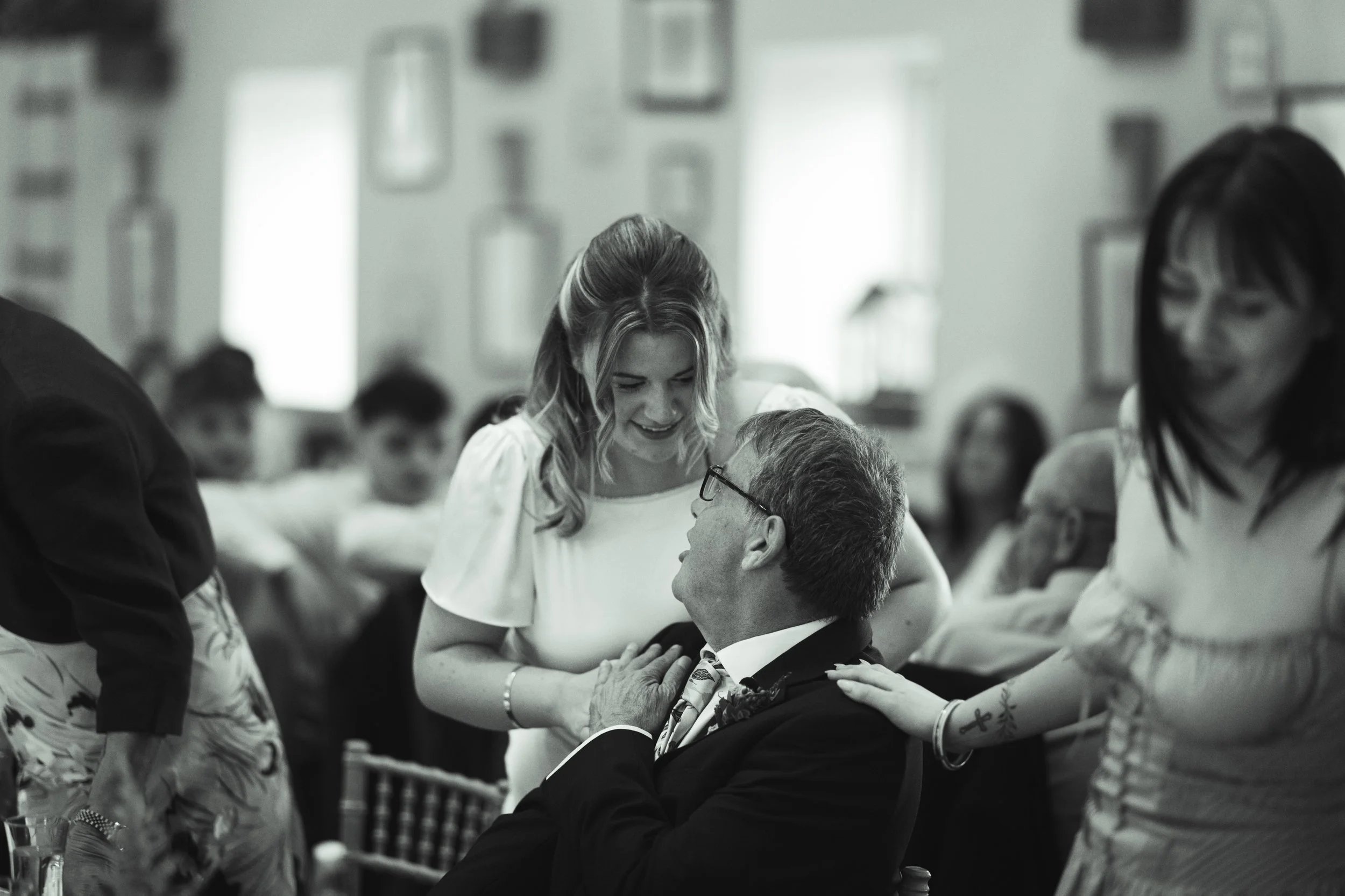A woman and an elderly man sharing a joyful moment at a social gathering, with other guests in the background.