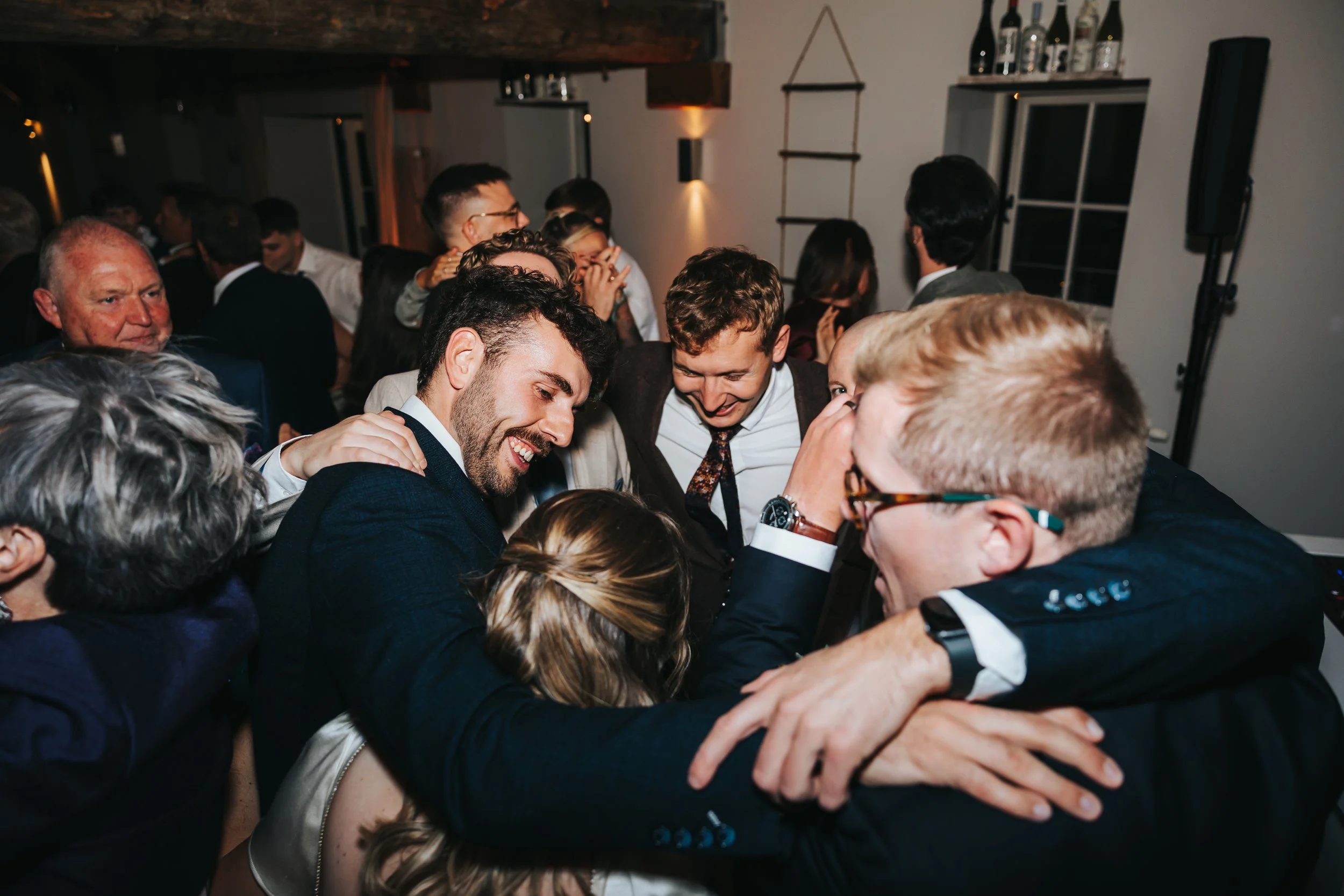 A group of people at a celebration, hugging and smiling in a crowded room.