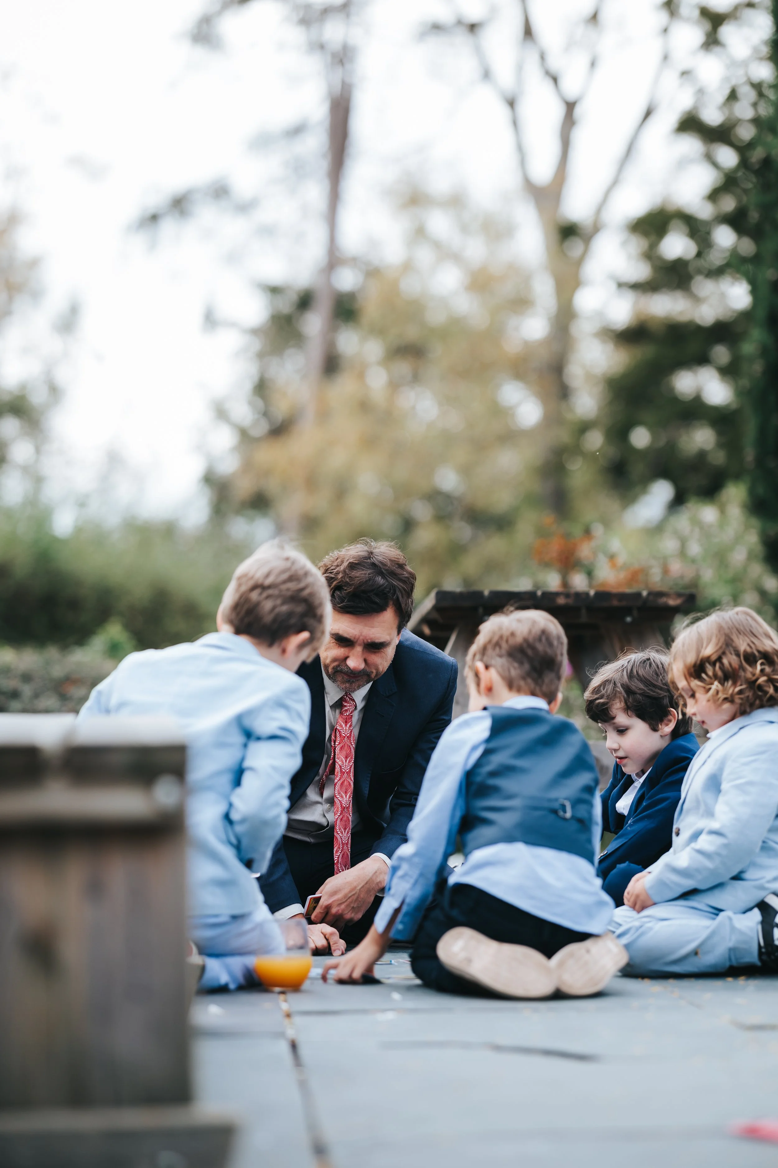 A man in a suit and five children sitting on the ground outdoors, engaged in a group activity or discussion.