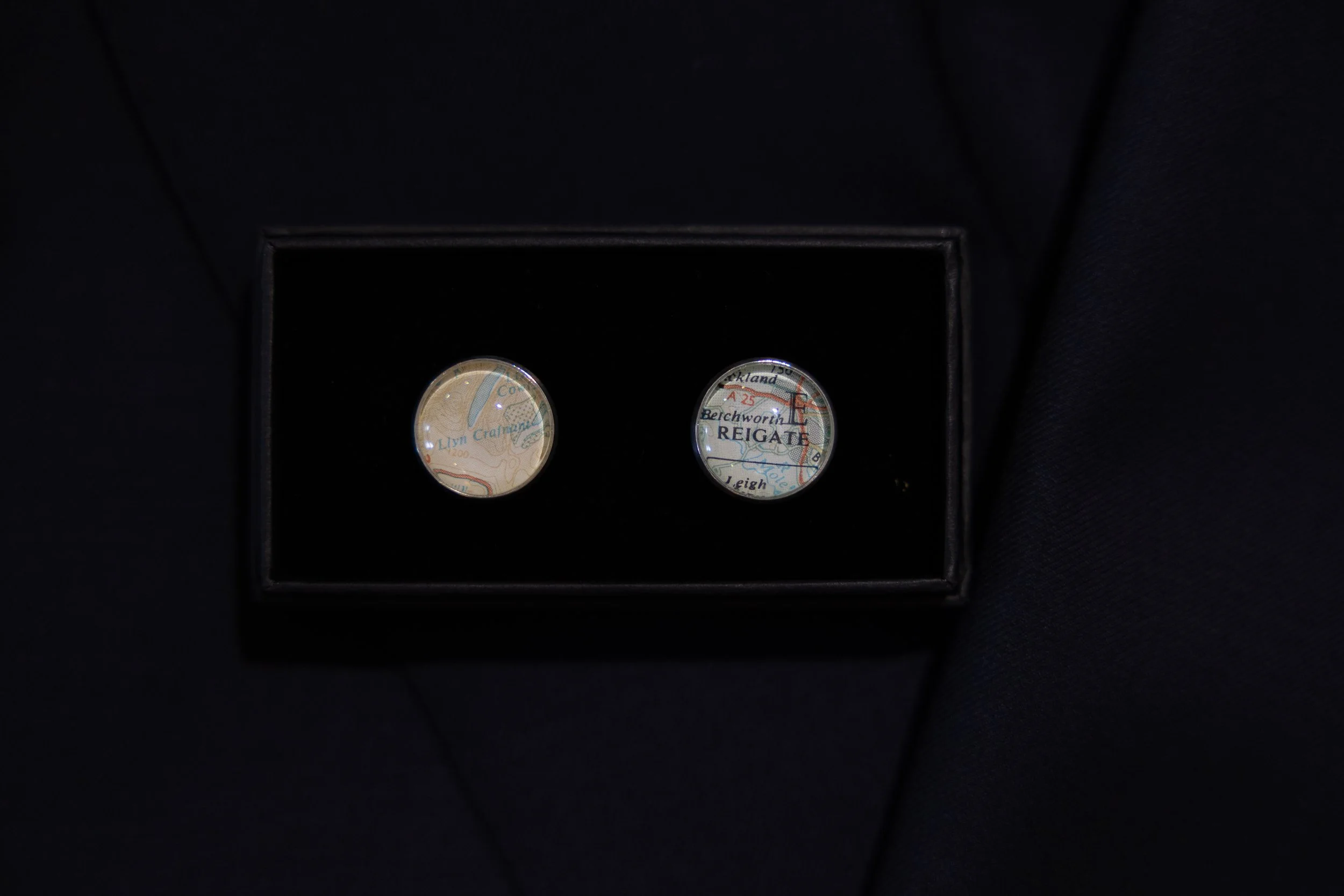 Pair of cufflinks with map design, placed in a black jewelry box.