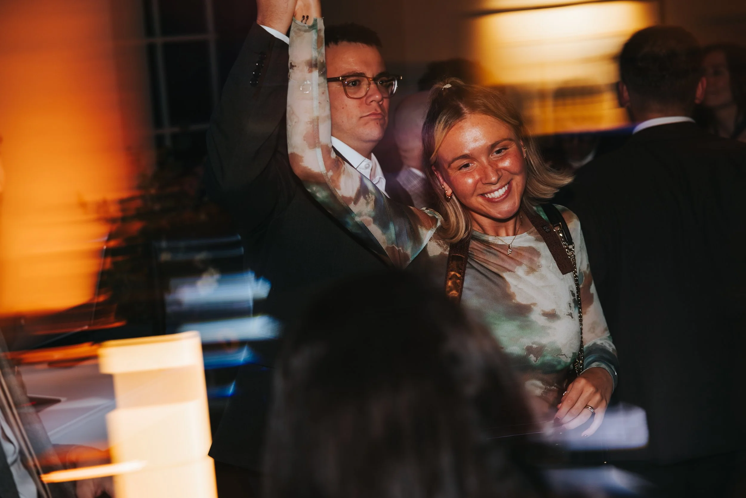 A man and woman dancing at a party or event, with the man raising his arm and the woman smiling.