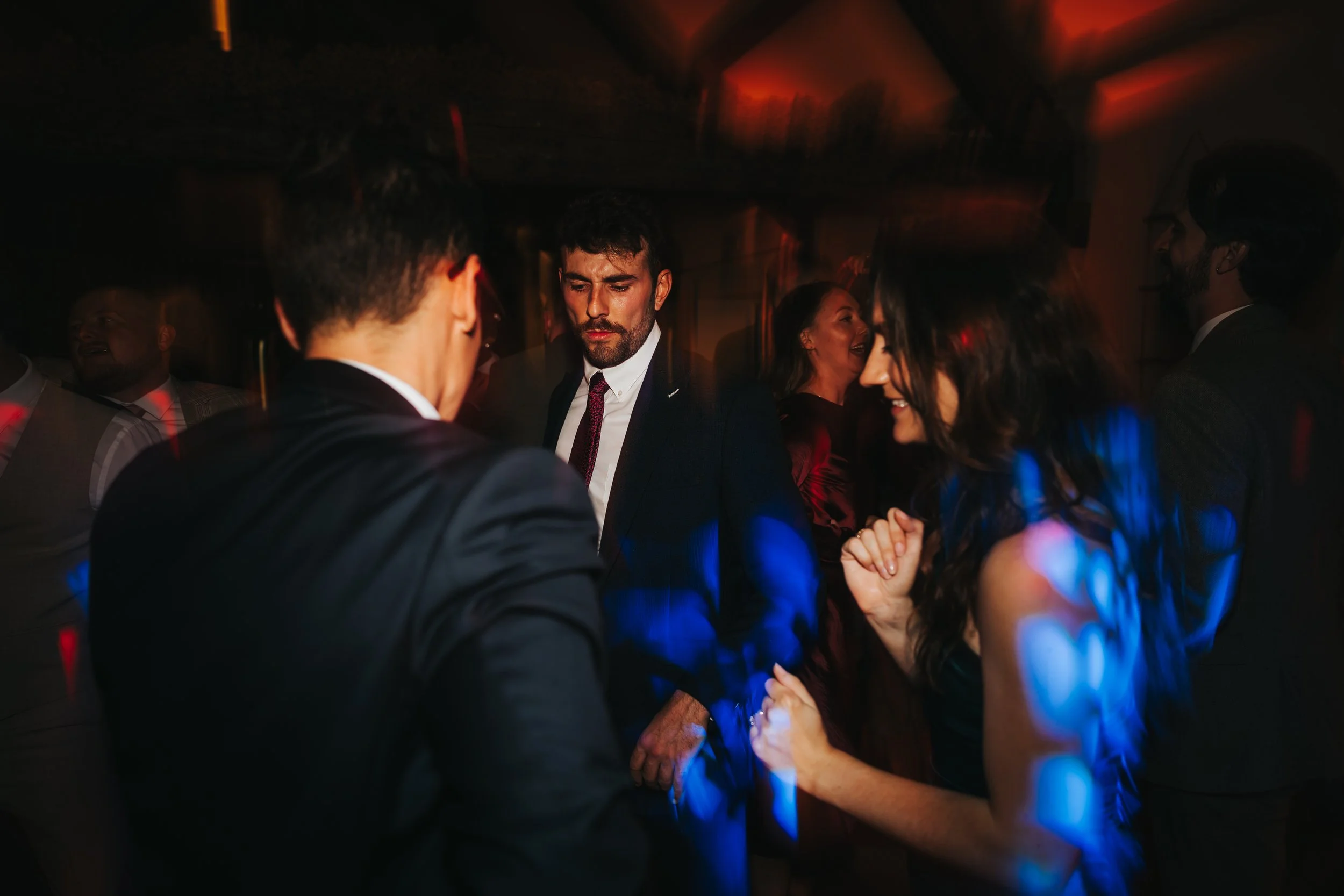 People dancing and socializing at a party or celebration in a dimly lit room with colorful lights.