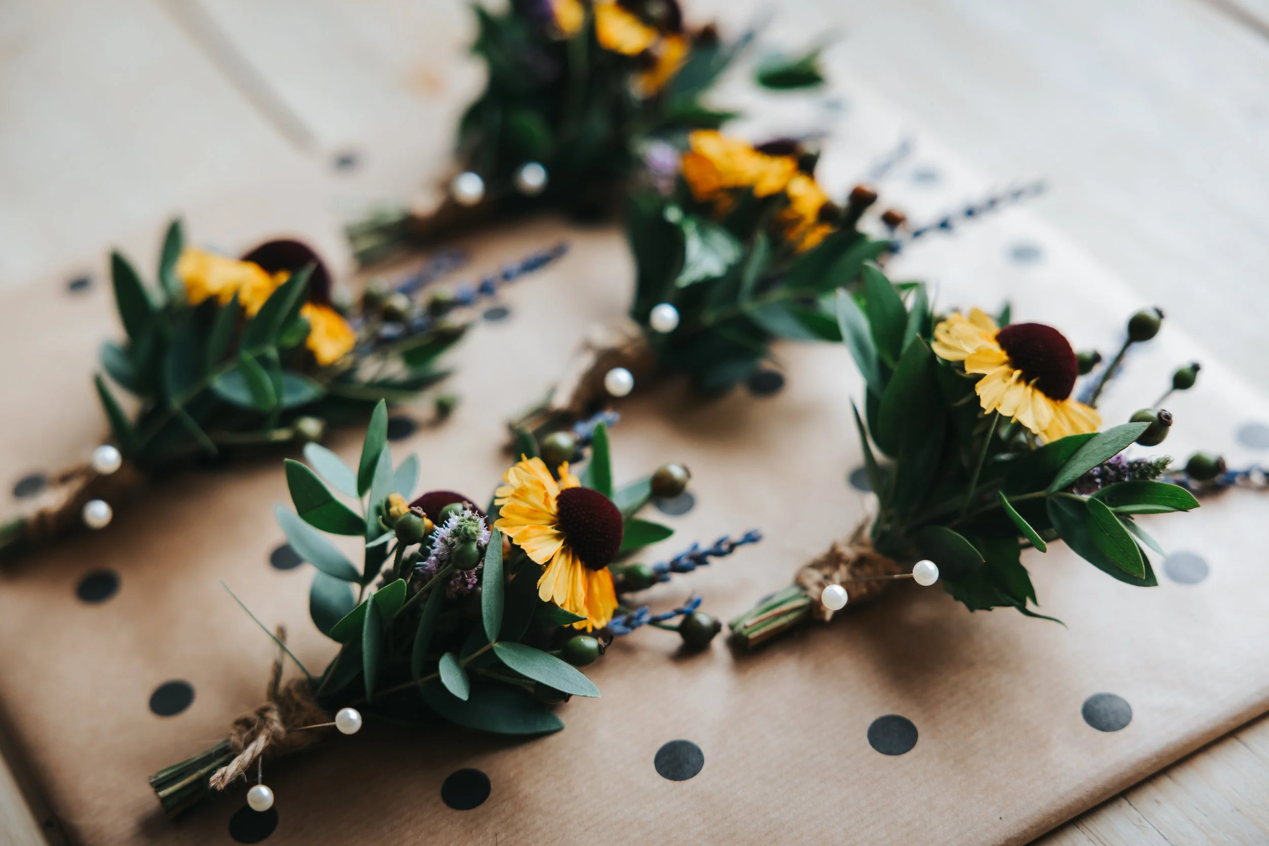 A floral crown with yellow flowers, green leaves, and white pearl accents placed on gift wrap with black polka dots.