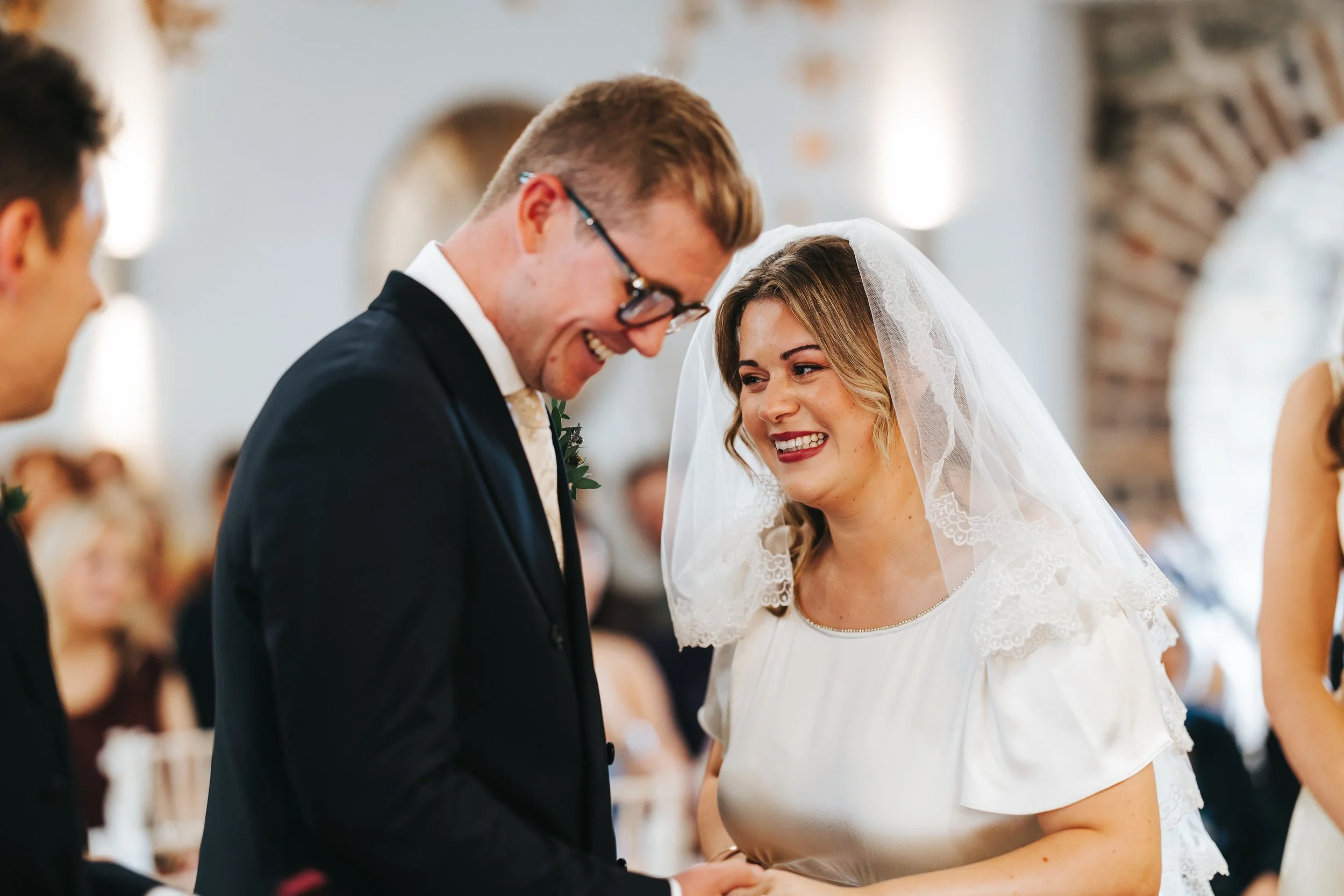A bride and groom smiling and holding hands during their wedding ceremony.
