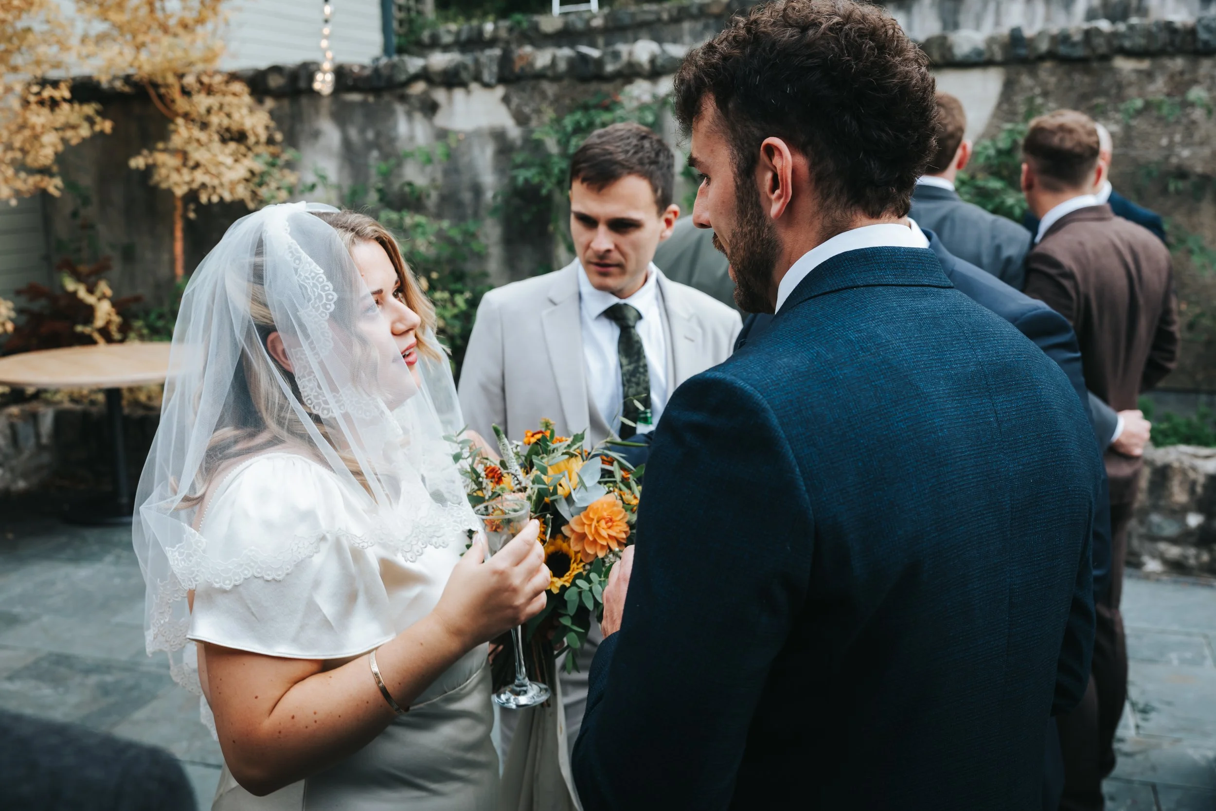 Bride and groom talking at a wedding reception, with guests in the background