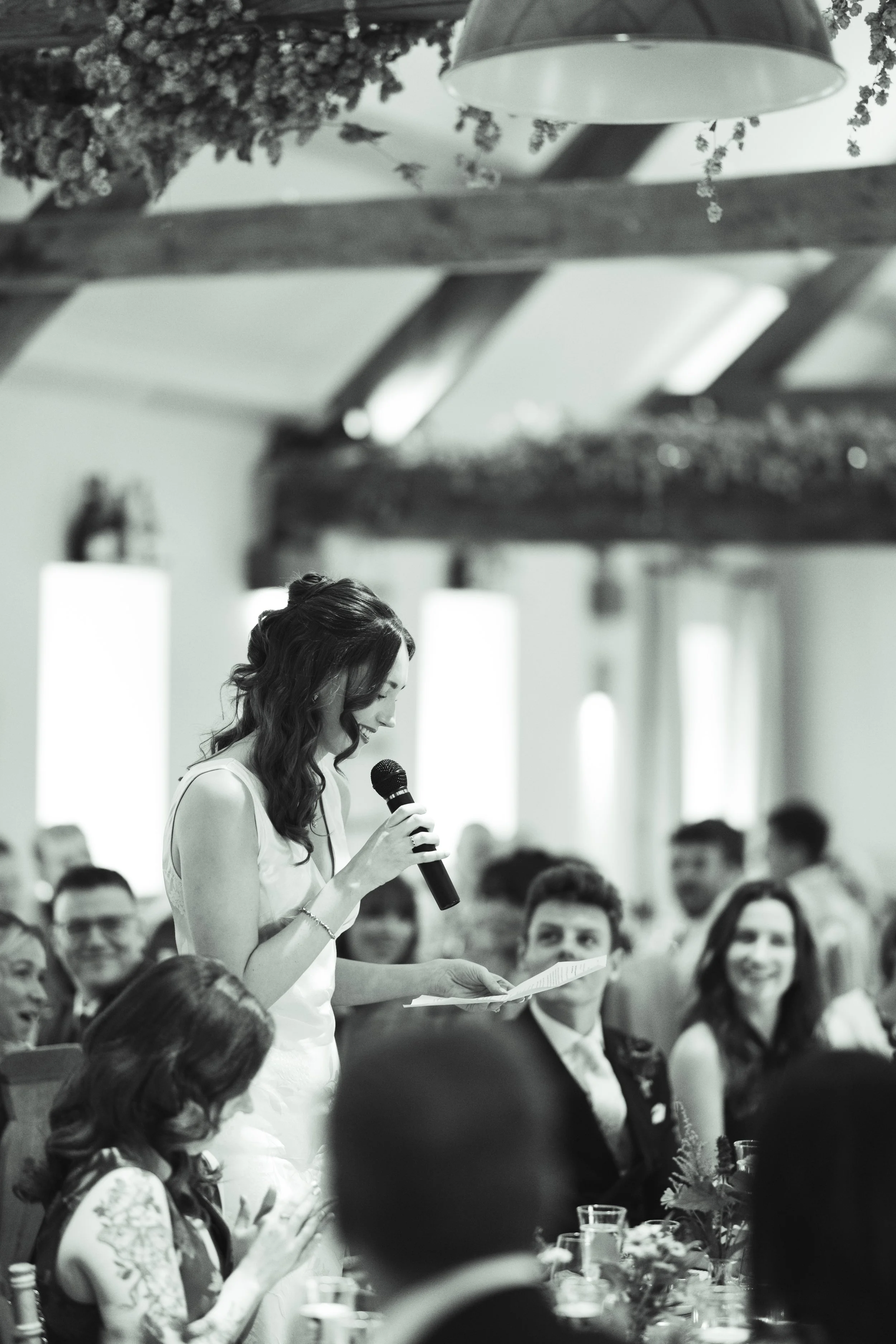 A woman giving a speech while holding a microphone at a formal event, seated among other guests.
