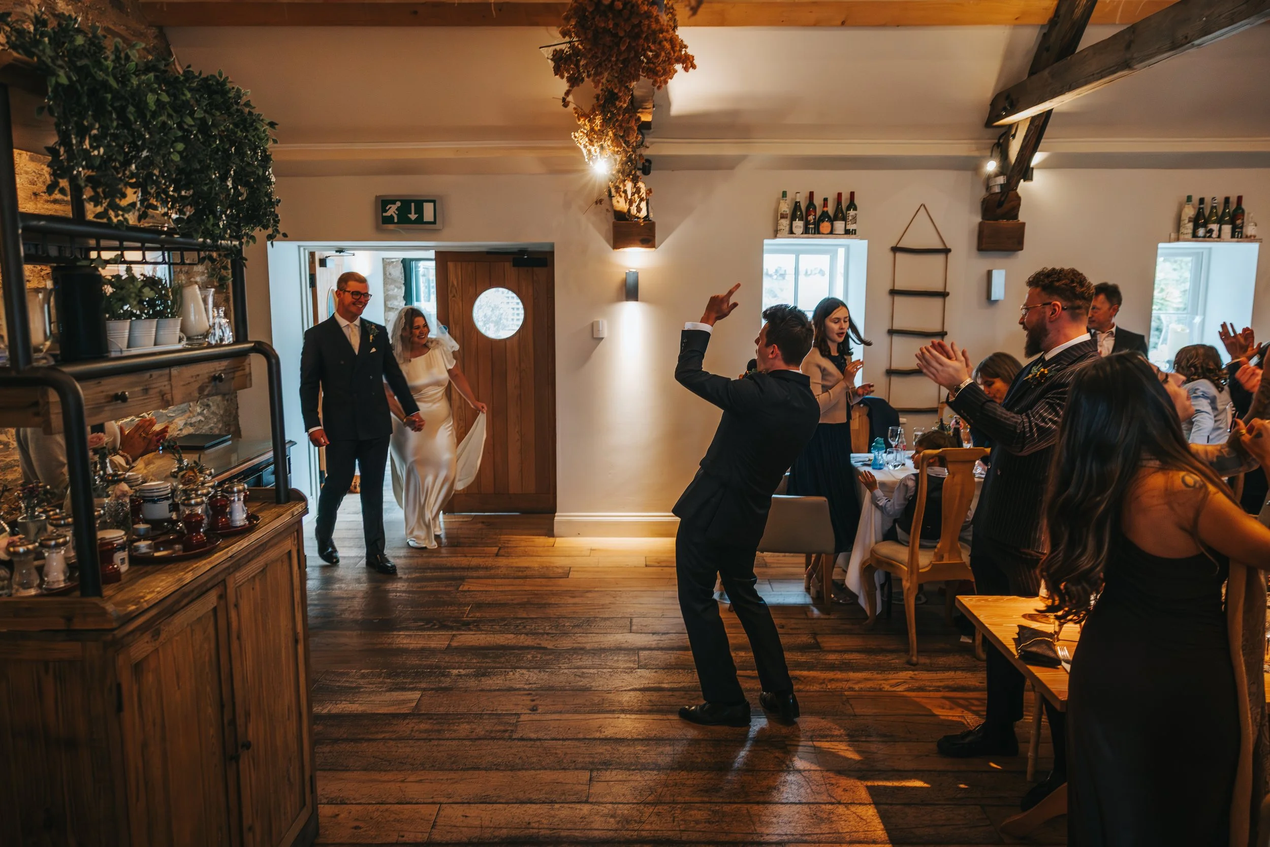 Wedding reception with bride and groom entering as guests cheer and clap.
