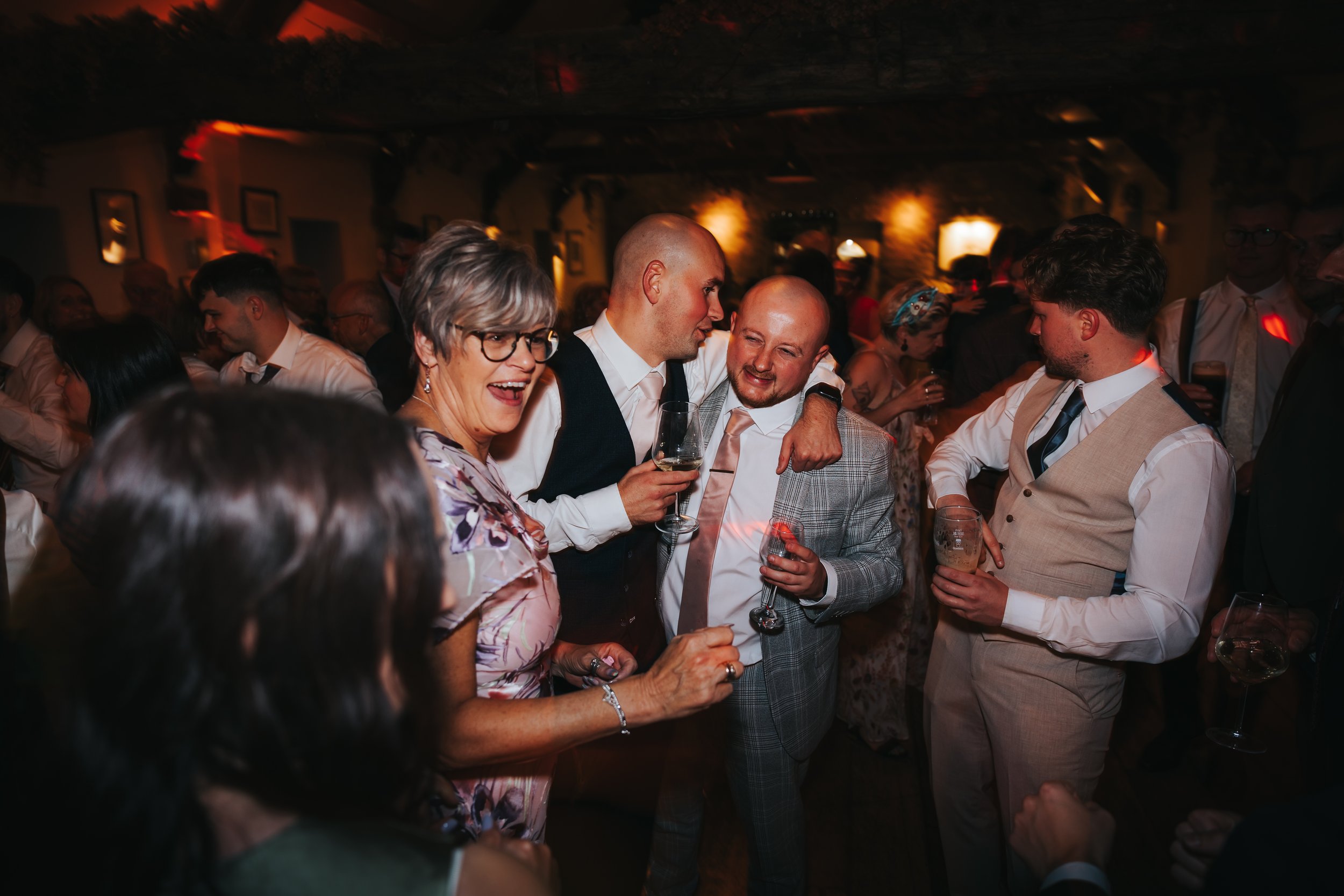 Group of people dancing and celebrating at a party or wedding reception in a dimly lit indoor venue.
