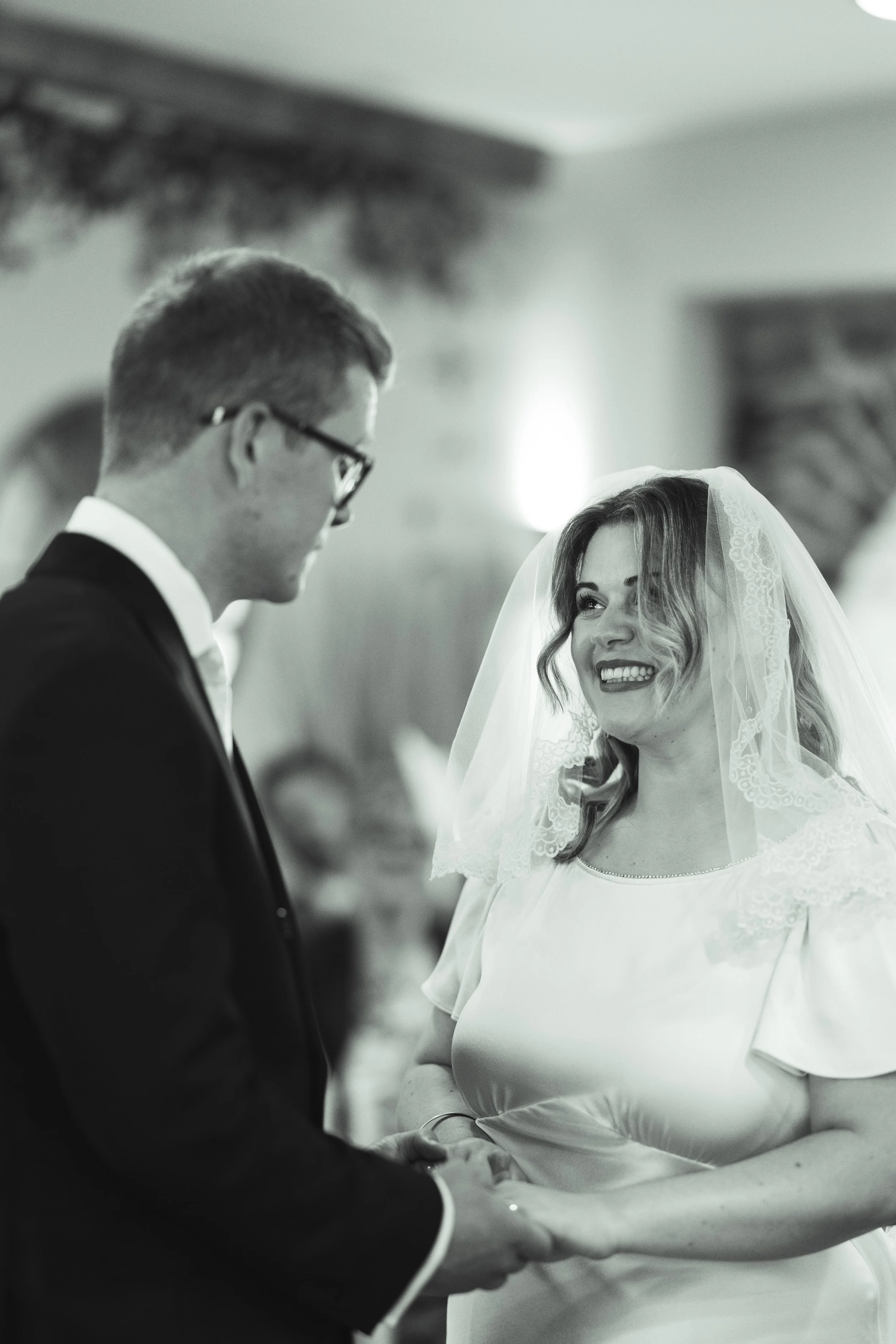 A bride and groom holding hands during their wedding ceremony, smiling at each other.
