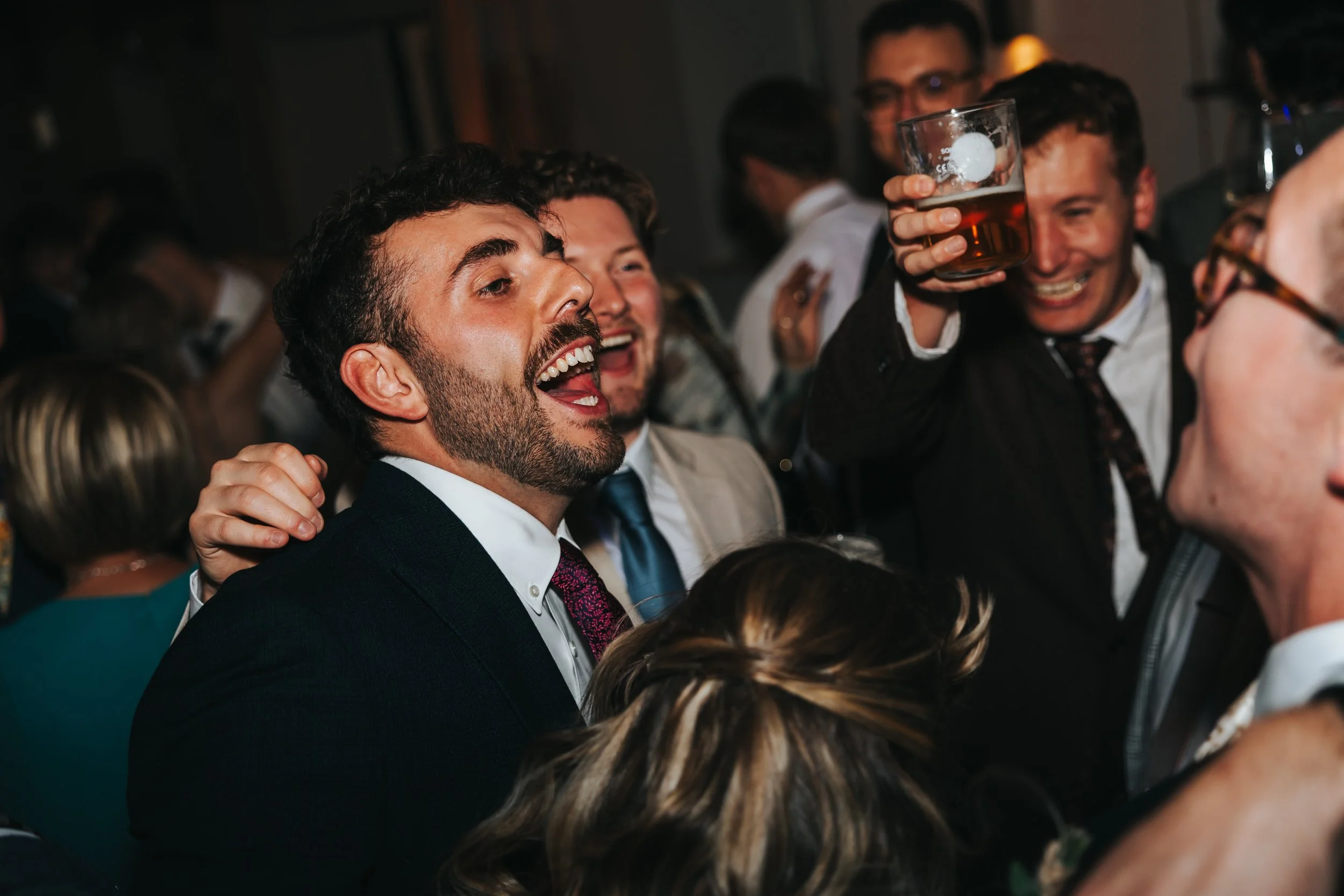 Group of people celebrating, smiling, and raising glasses in a party or event, with one man holding a drink close to his face.