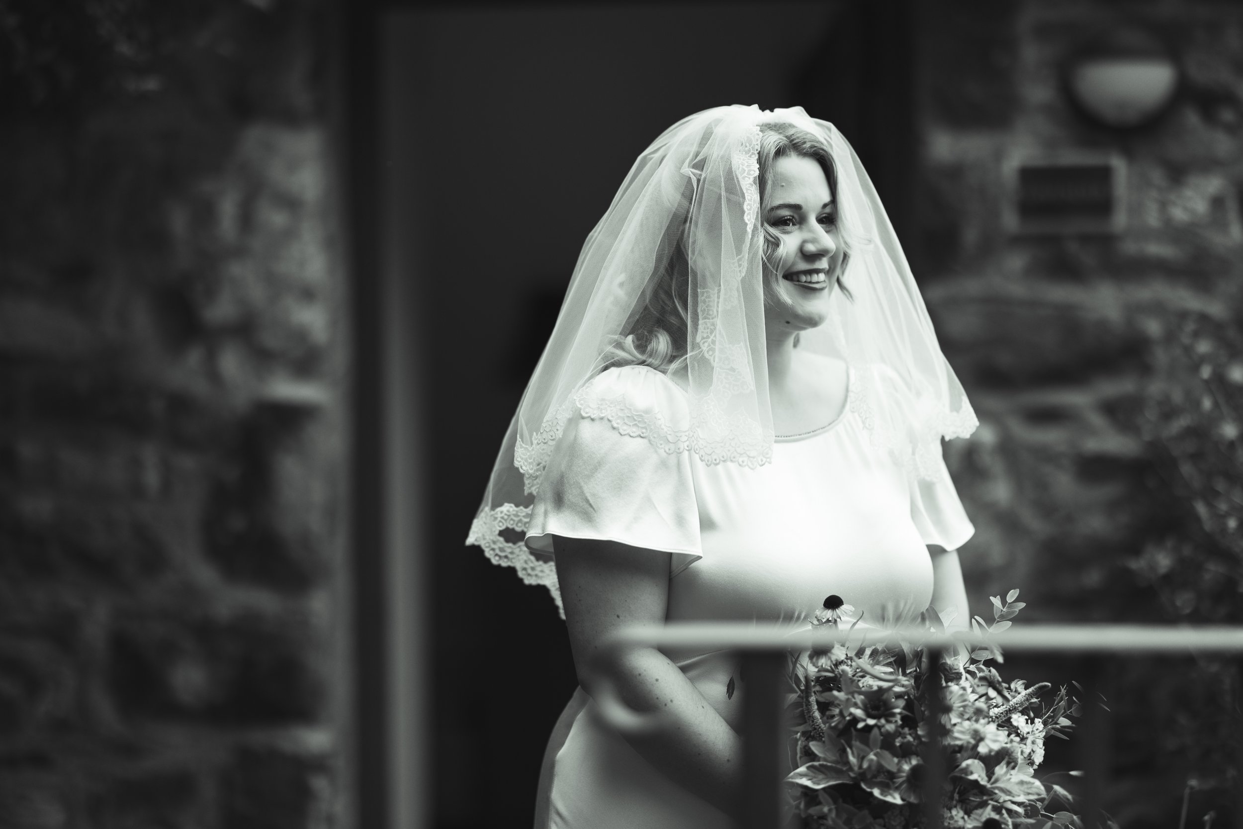 Black and white photo of a smiling bride wearing a veil and holding a bouquet of flowers.
