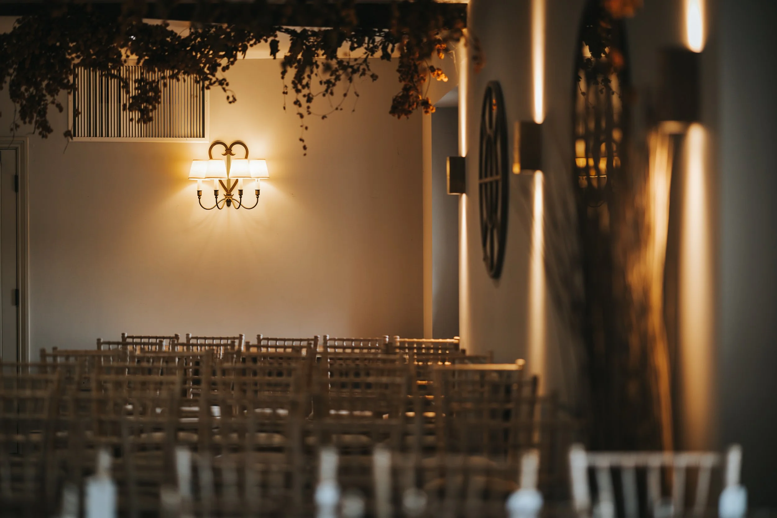 Empty dining area with wooden chairs, a wall-mounted chandelier, and decorative wall clocks.