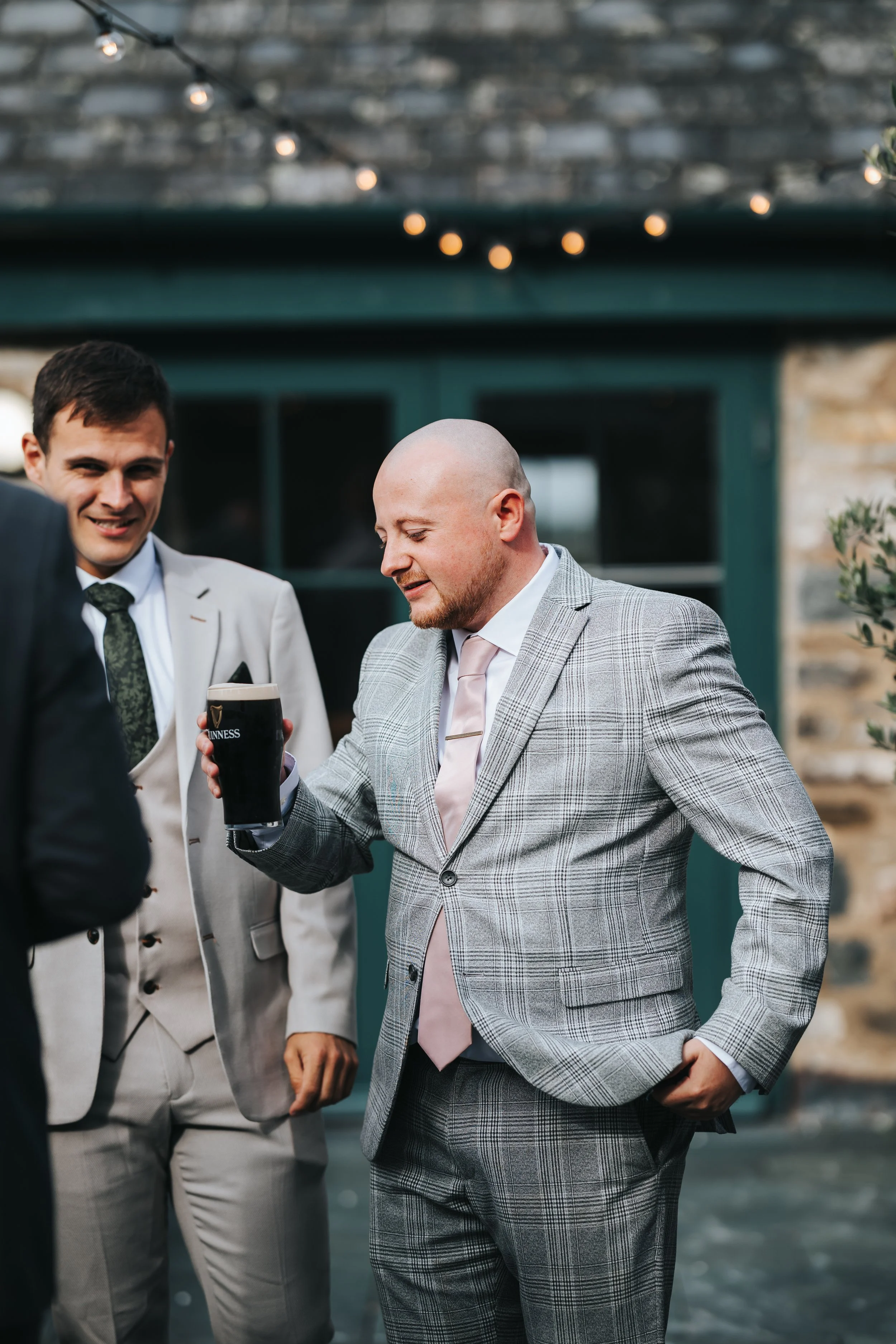 Three men in suits enjoying drinks at an outdoor gathering, with one holding a pint of Guinness.